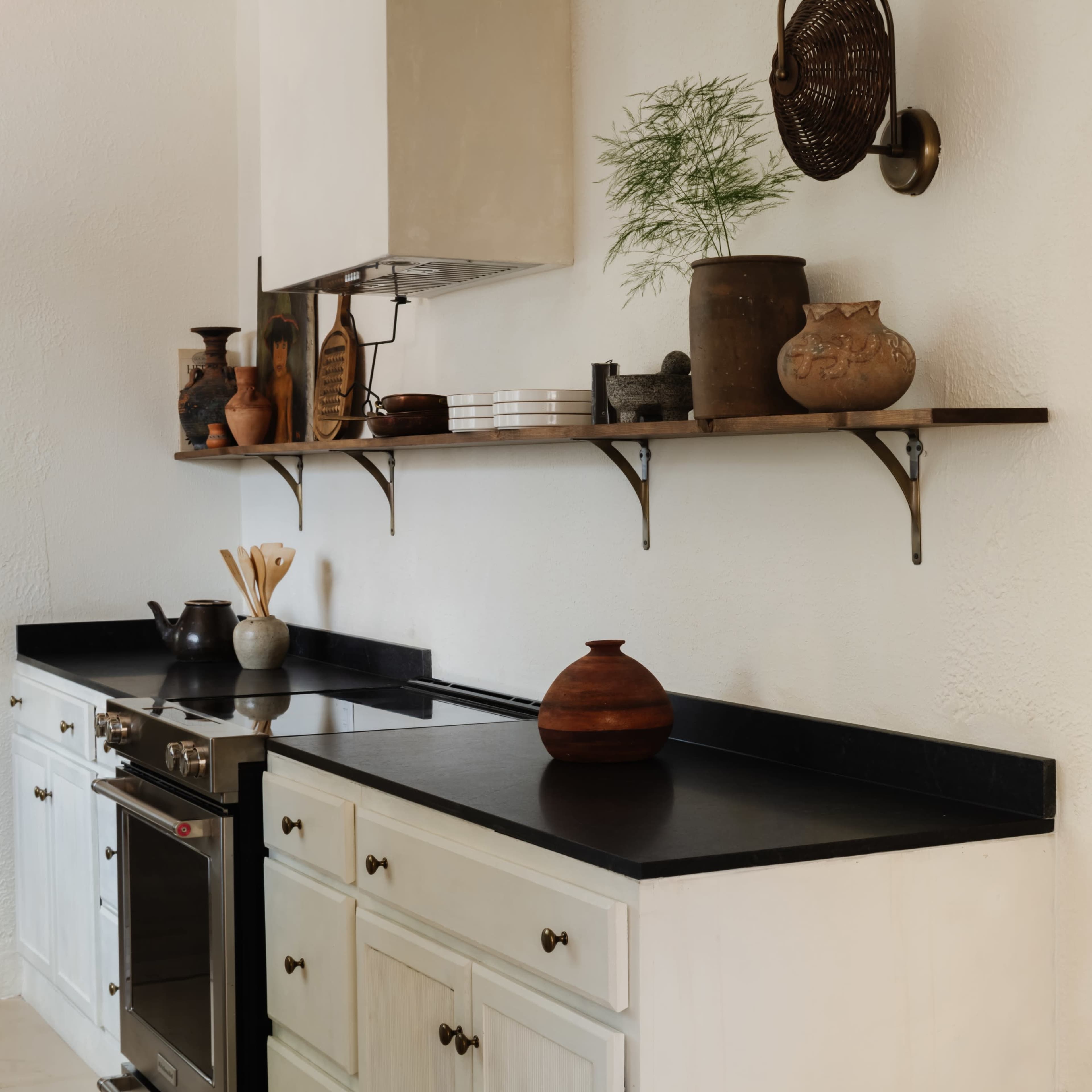 A modern kitchen with white cabinetry, a black countertop, and various decorative items arranged on a wooden shelf.