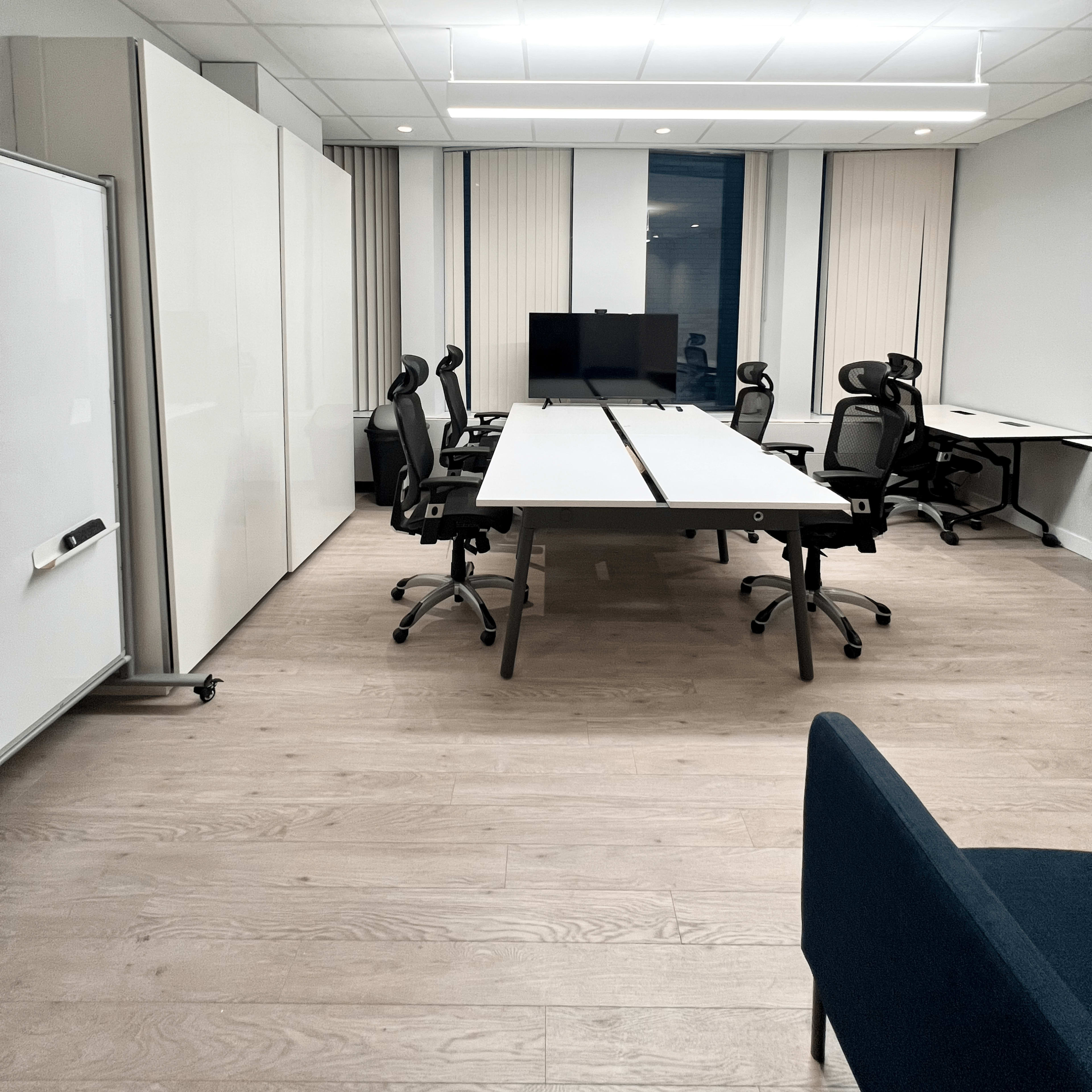 A modern office space with multiple desks, ergonomic chairs, a large screen, and a whiteboard.