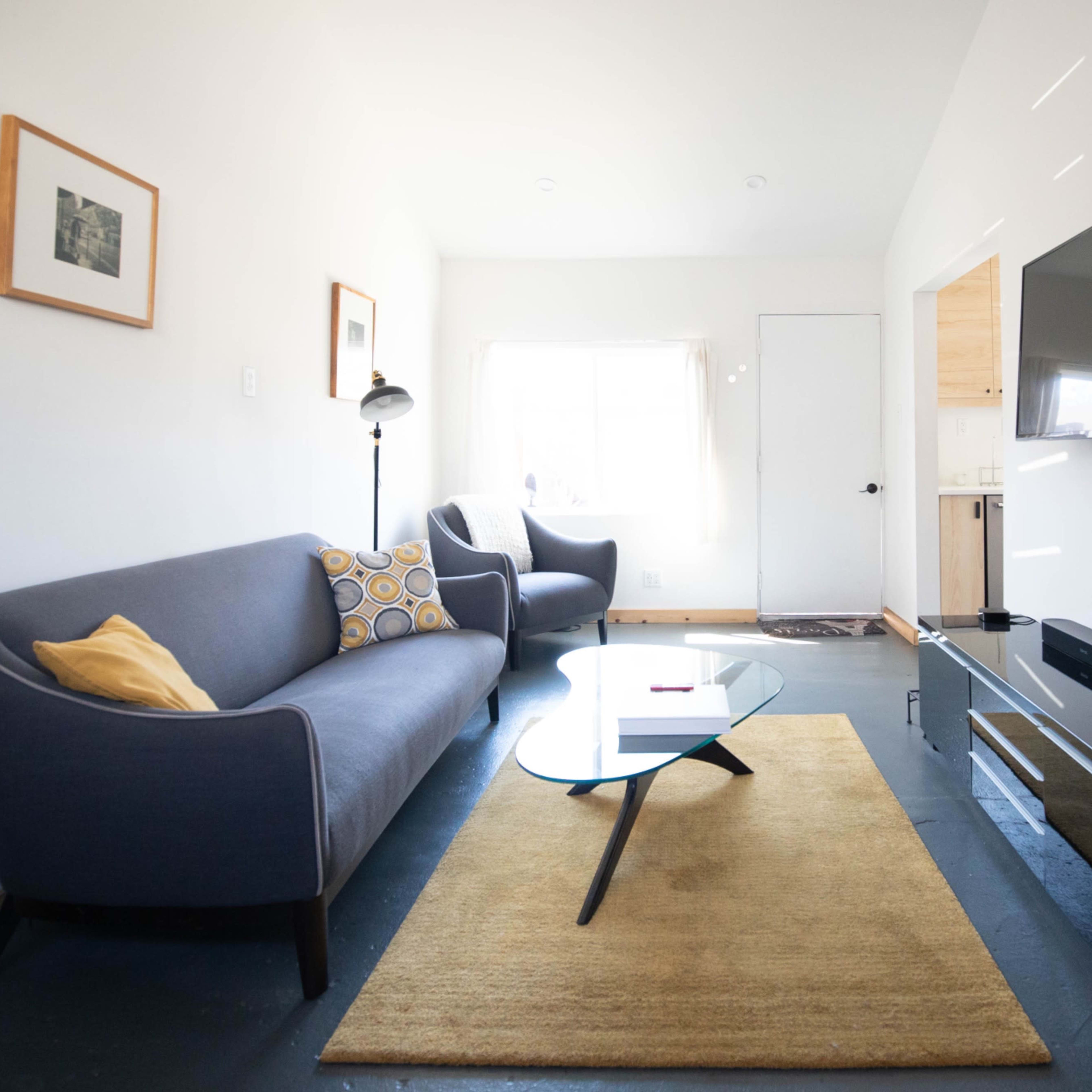A living room with a gray sofa, a round coffee table, a flat-screen TV mounted on the wall, and a beige area rug.