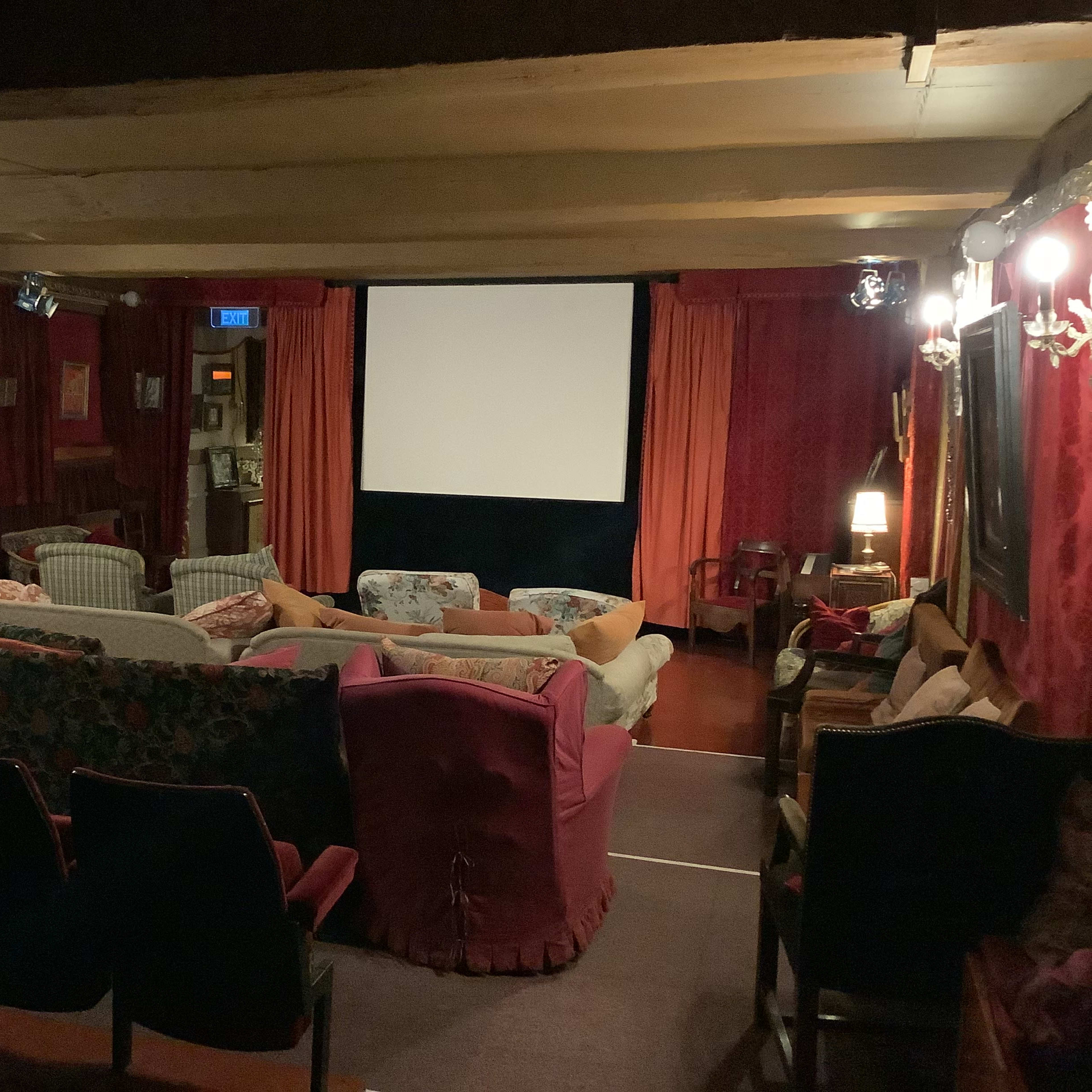 A cozy home theater with various sofas and chairs arranged in front of a large screen, framed by dark curtains and decorative wall sconces.