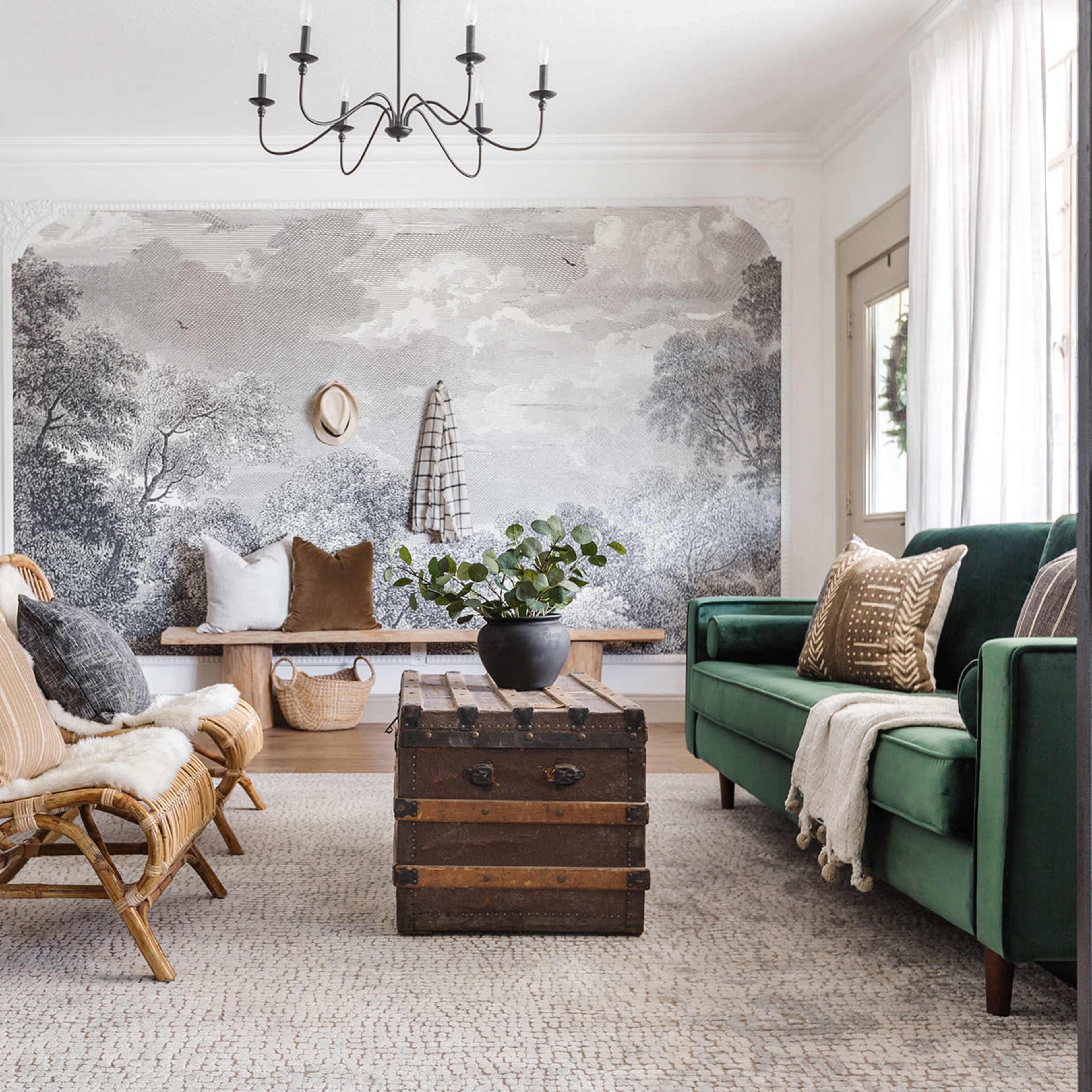 The living room features a green sofa, a wooden coffee table, and rattan chairs, with a large scenic wallpaper mural and natural light streaming in through the windows.
