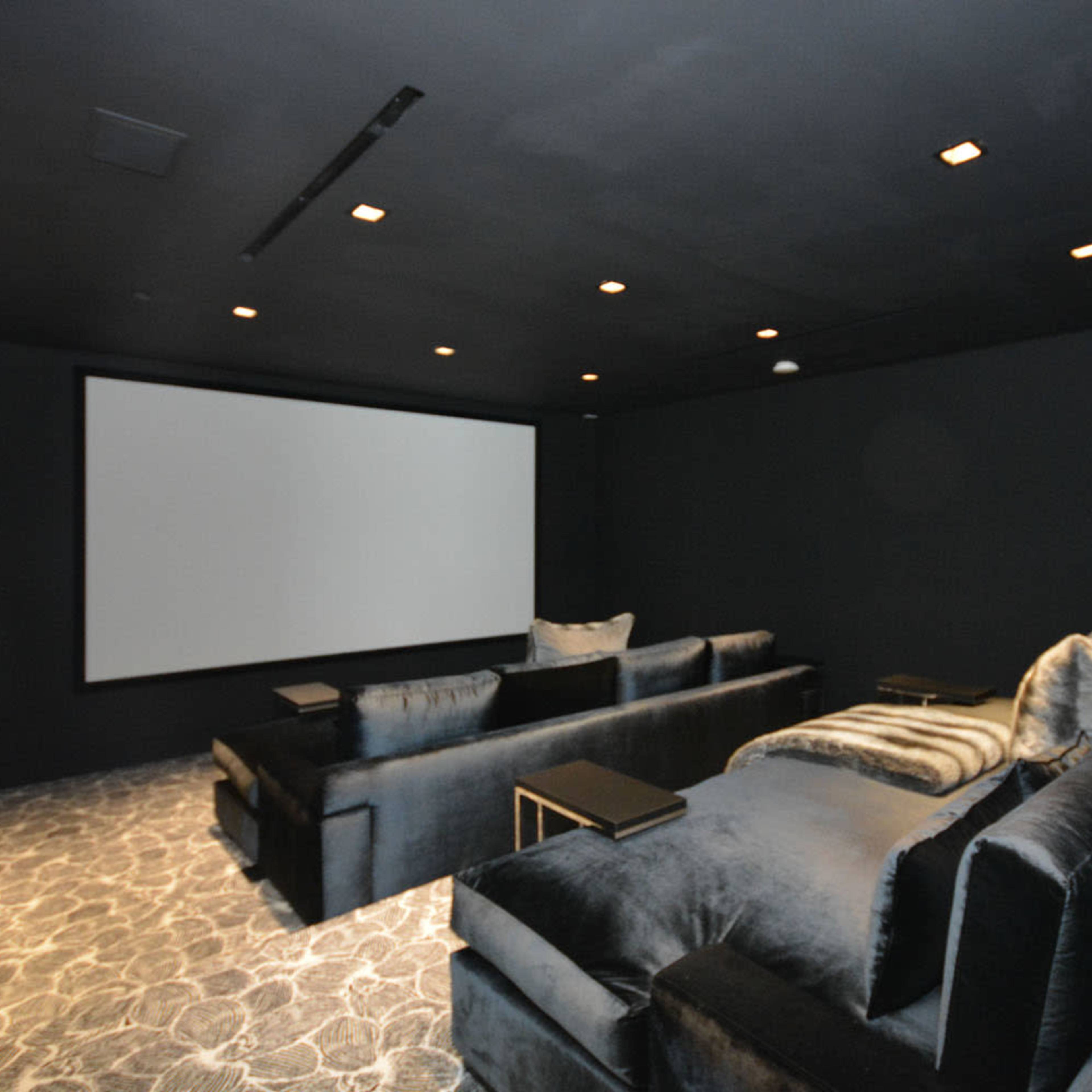 A darkened home theater room with a large screen, plush seating, and carpeted flooring.