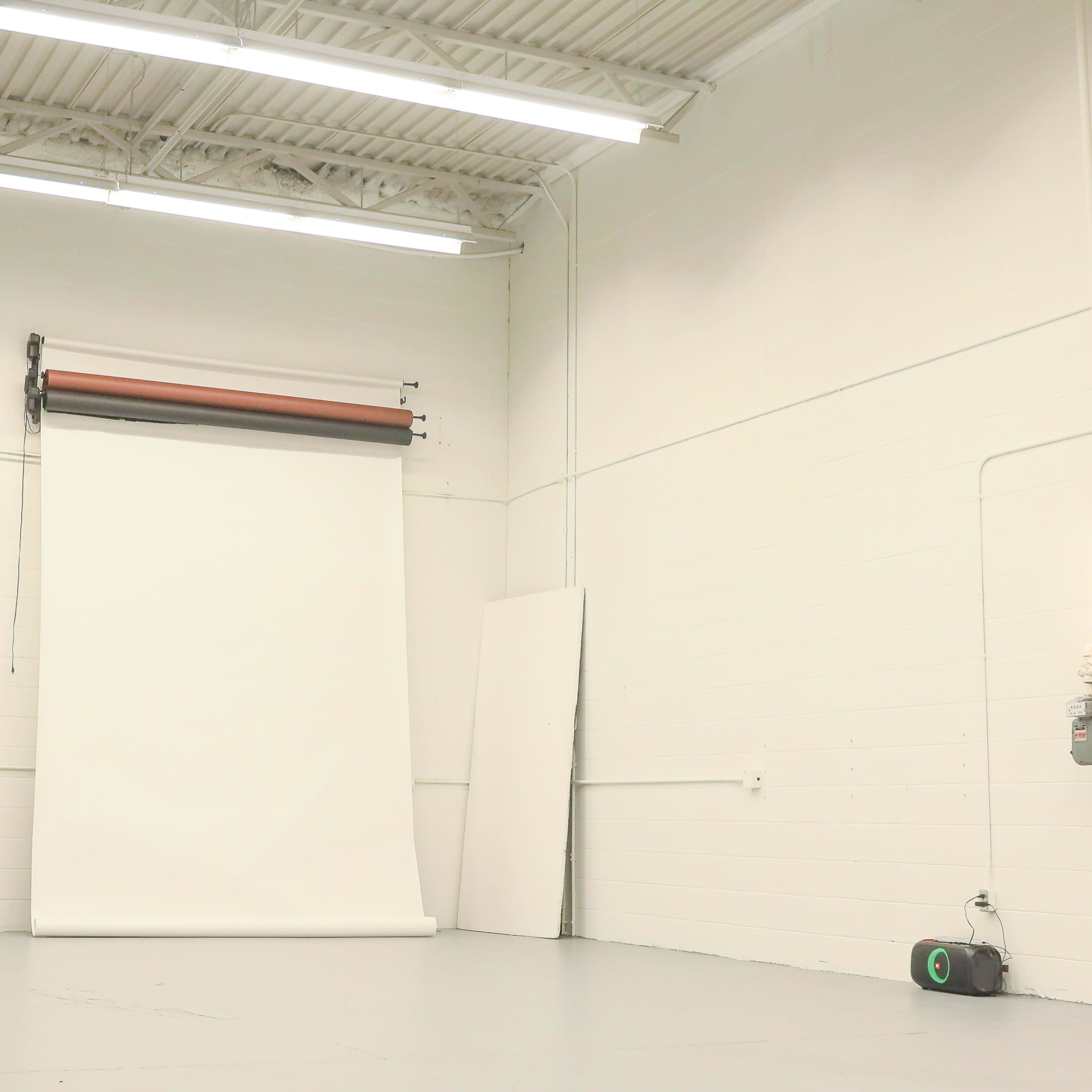 A large, empty photography studio with a white backdrop and industrial lighting.