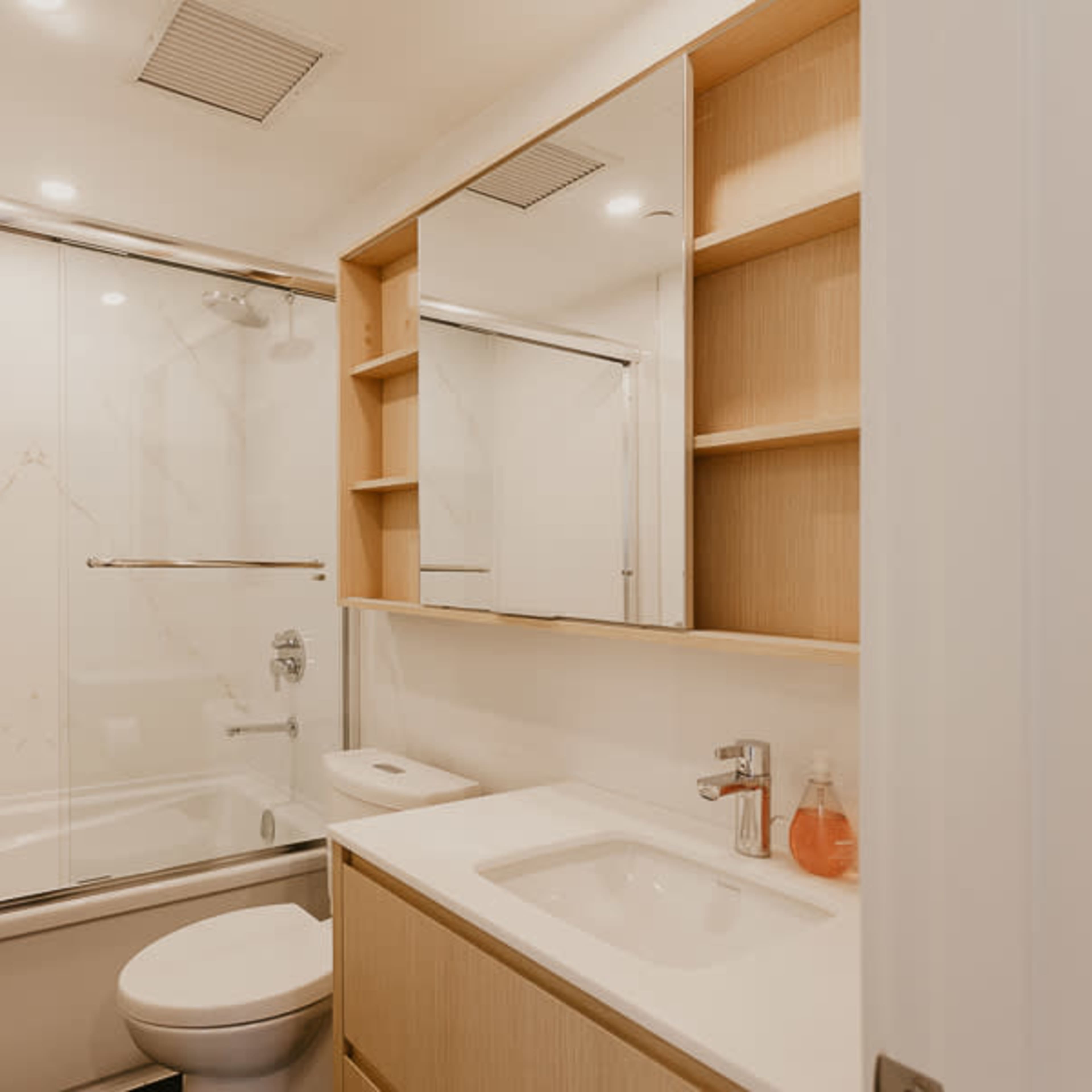 A modern bathroom featuring a glass shower, a wall-mounted mirror, and wooden shelves beside a sink and toilet.