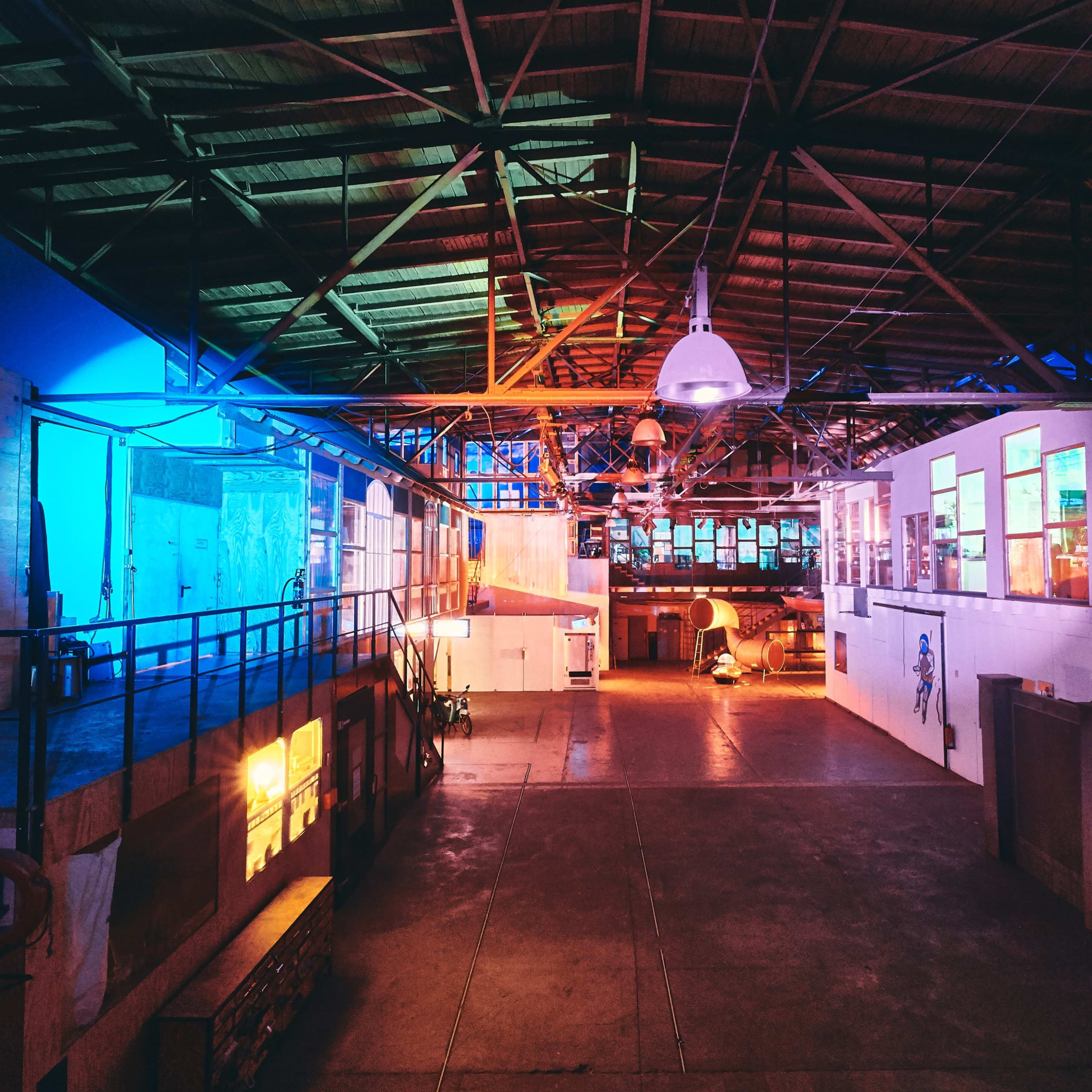 A spacious industrial interior with colorful lighting, featuring sections of walls and large windows in a warehouse-like setting.