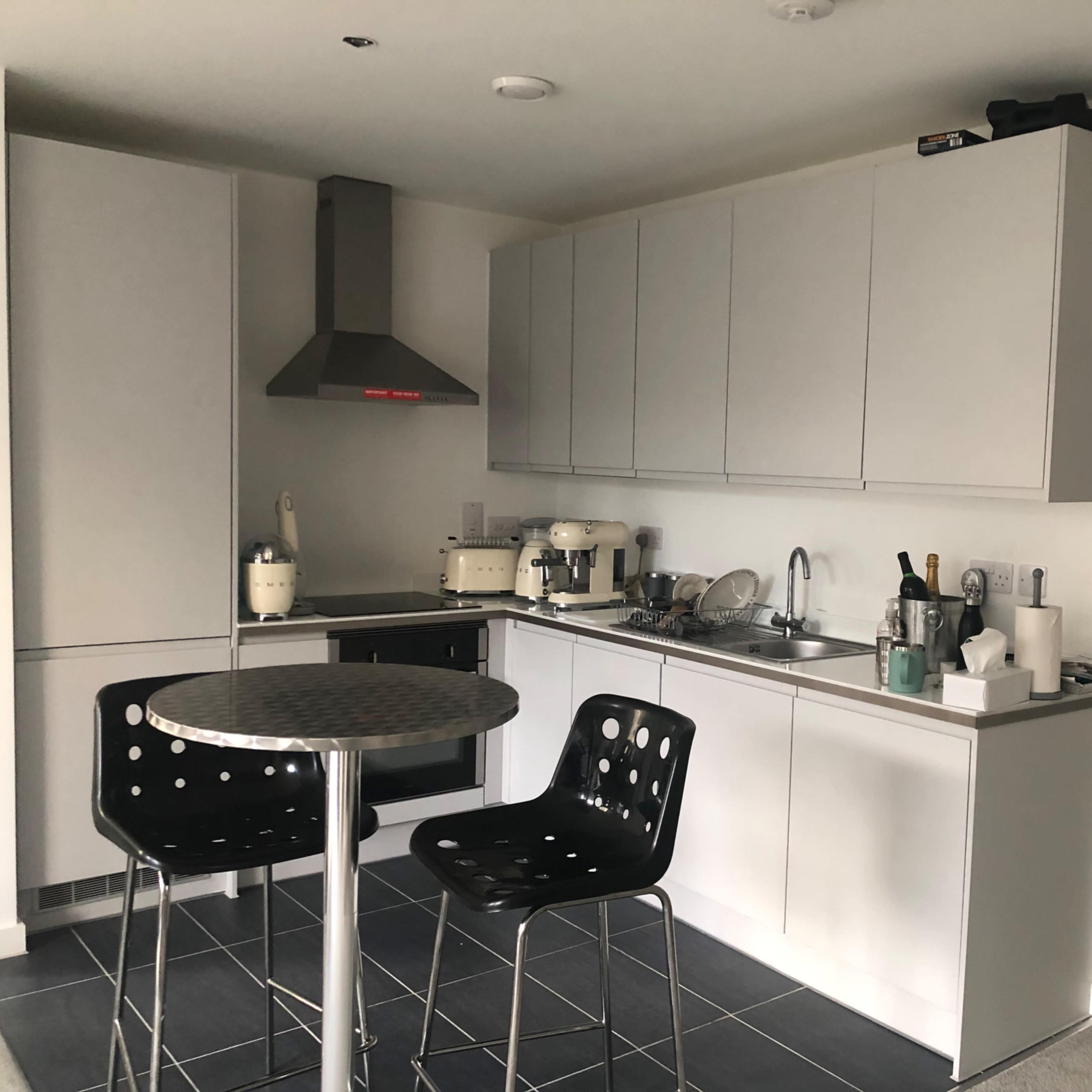 A modern kitchen featuring gray cabinets, a stainless steel range hood, and a round table with two black chairs.