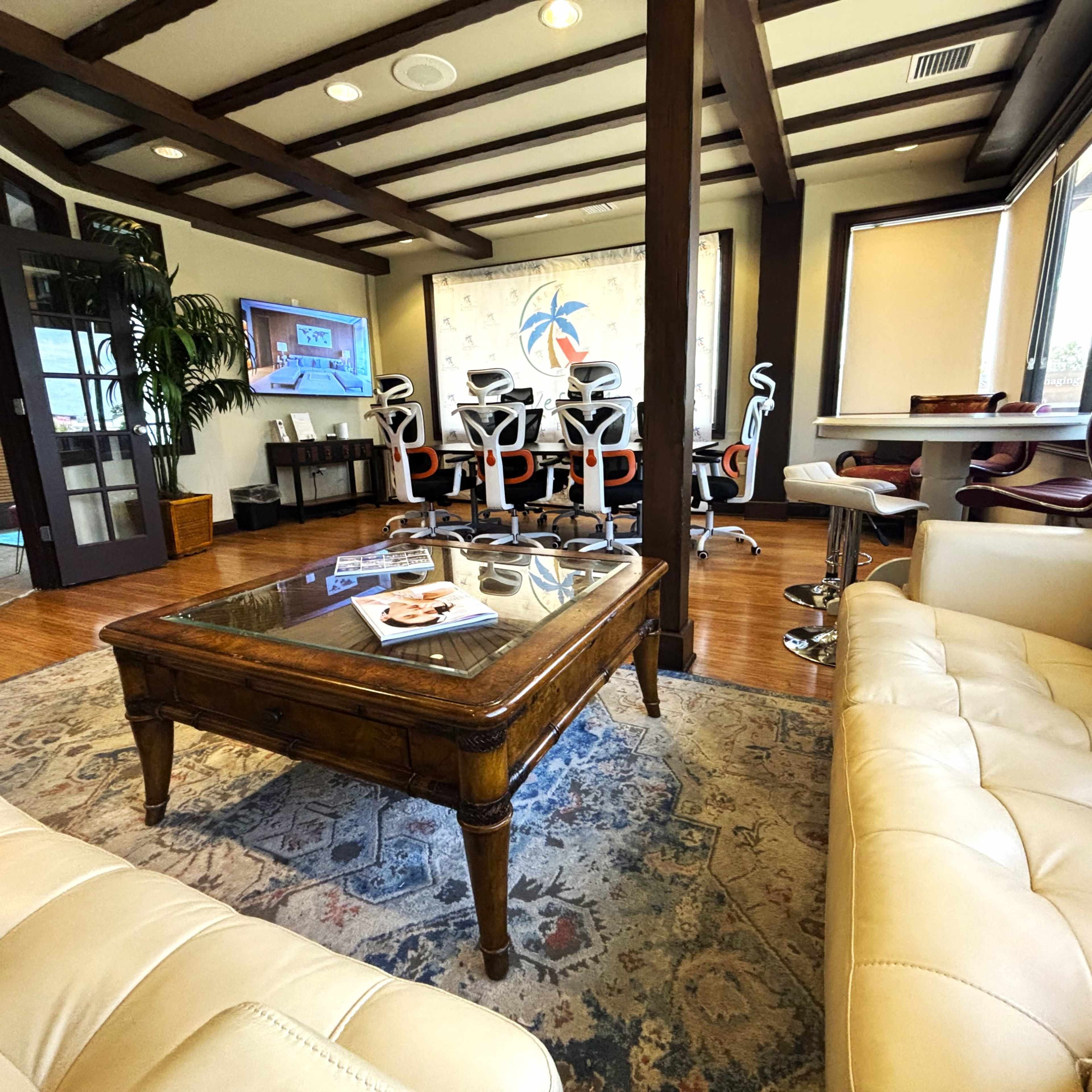 A modern office interior features a seating area with a coffee table, a large television, and several ergonomic chairs arranged around a conference table.