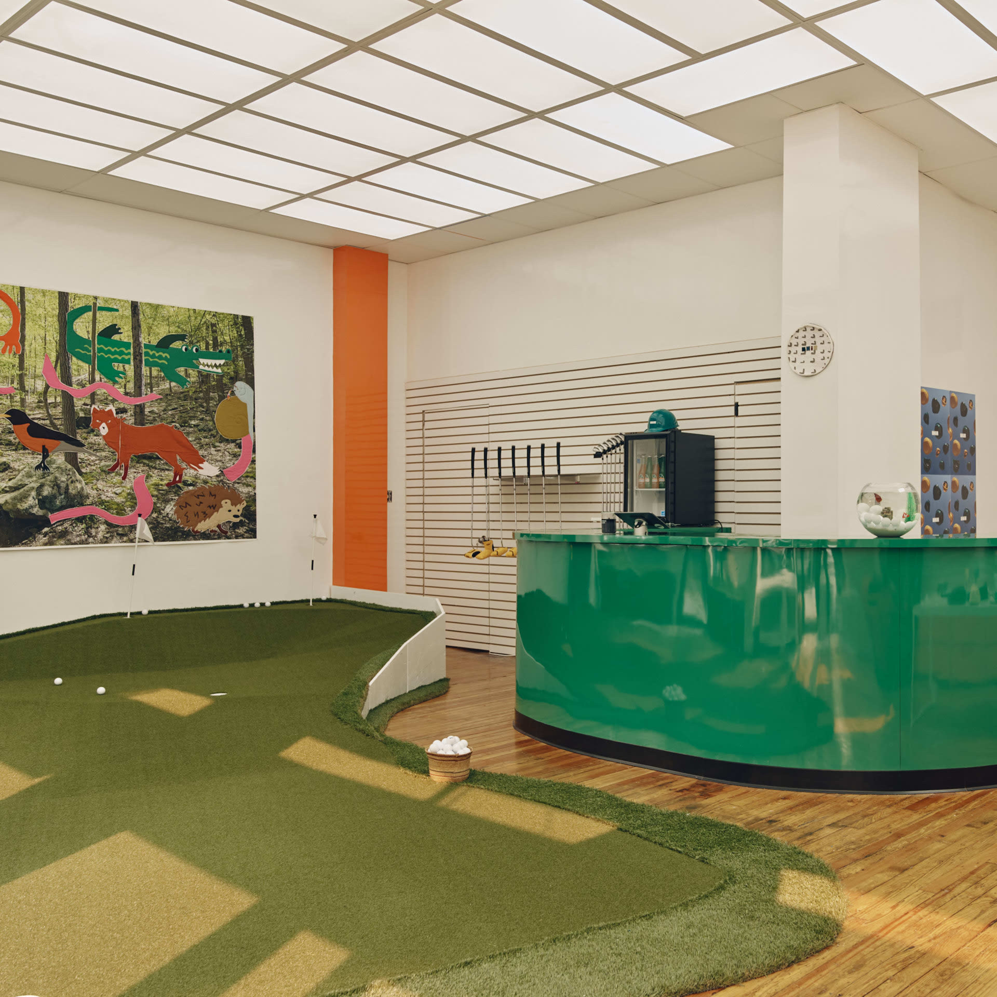 A modern interior featuring a green curved reception desk, a putting green area, and colorful wall art.