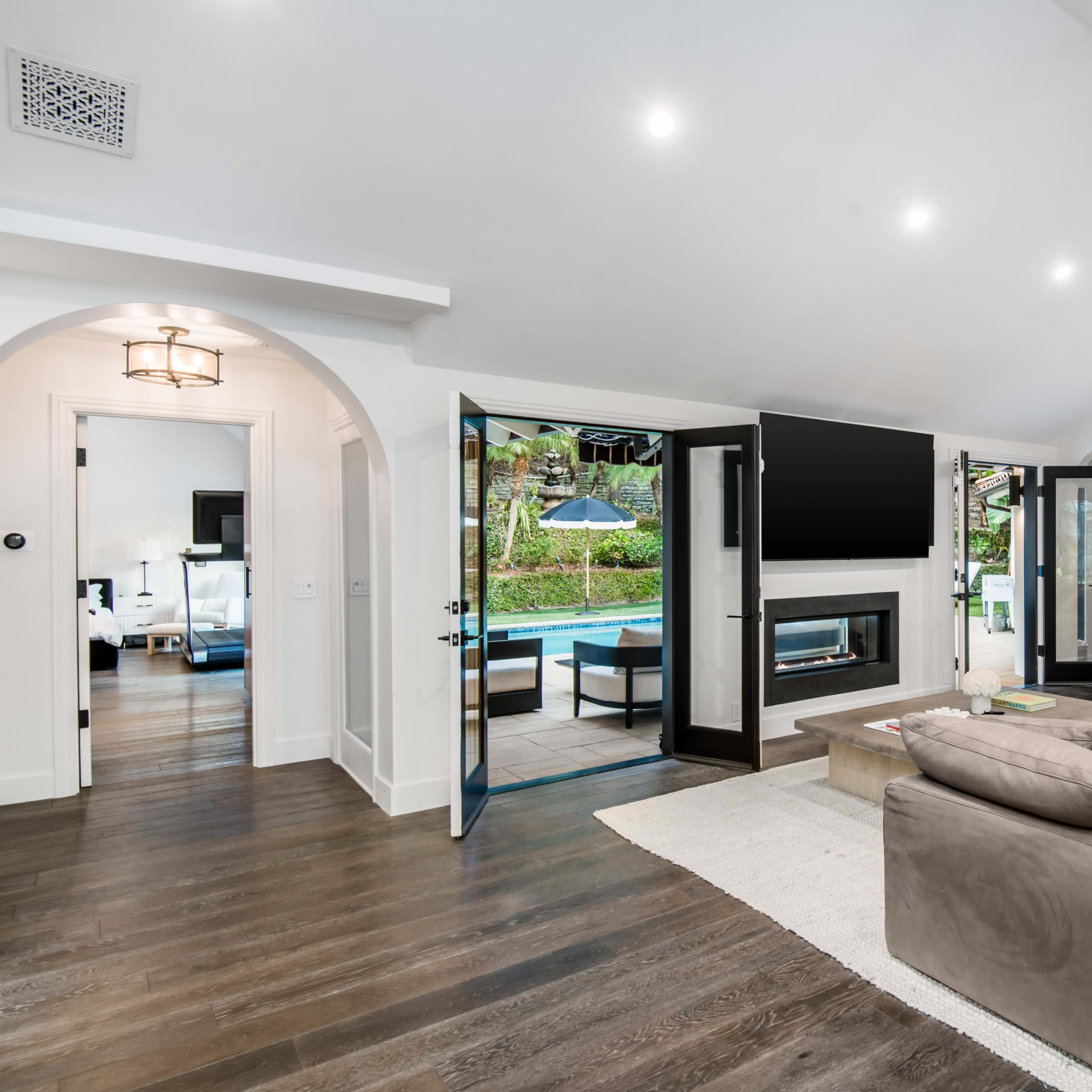 A modern living room with large open doors leading to a pool area, featuring a sectional couch and a fireplace.