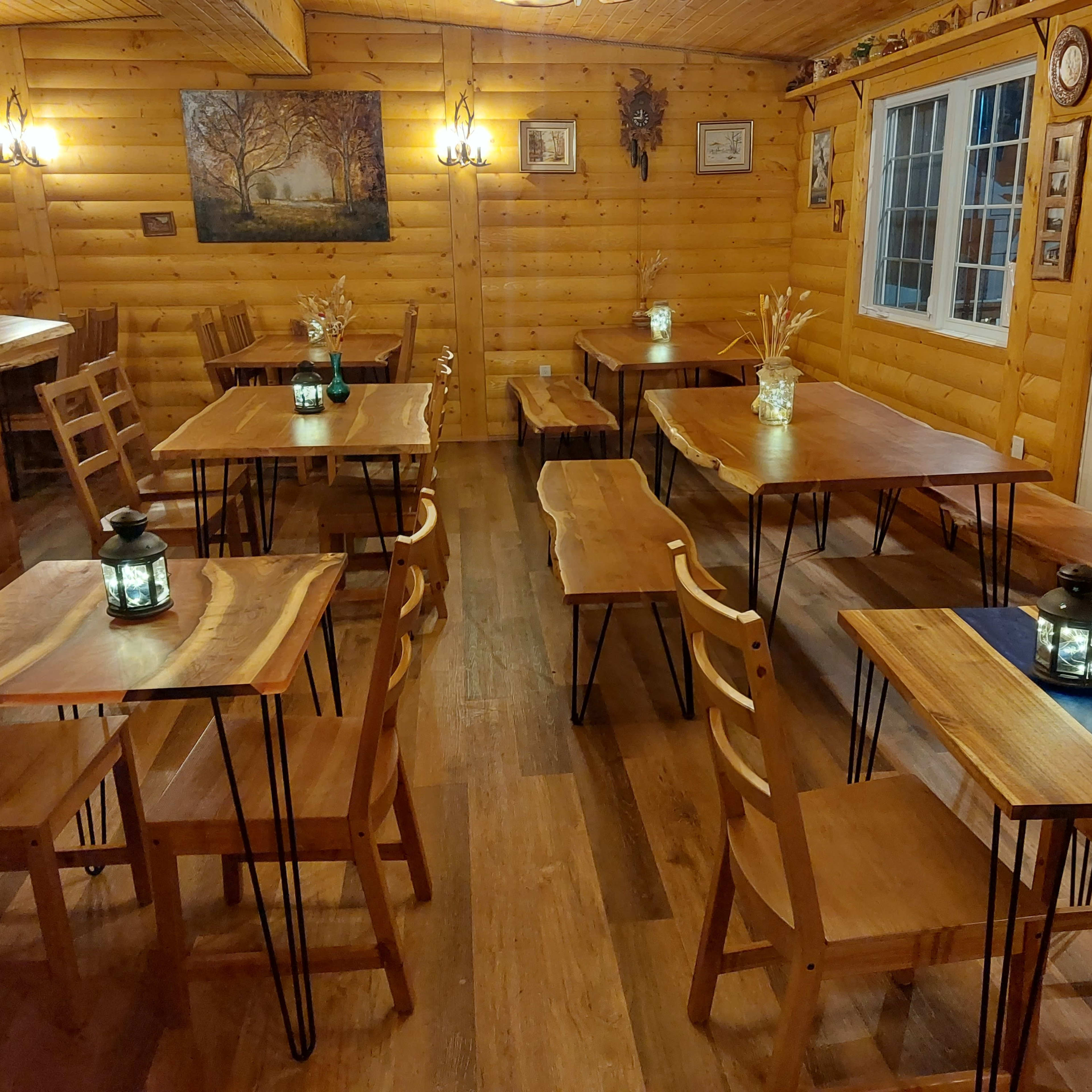 A wooden interior space with several tables and chairs arranged neatly around lanterns, along with a bar area and large windows.
