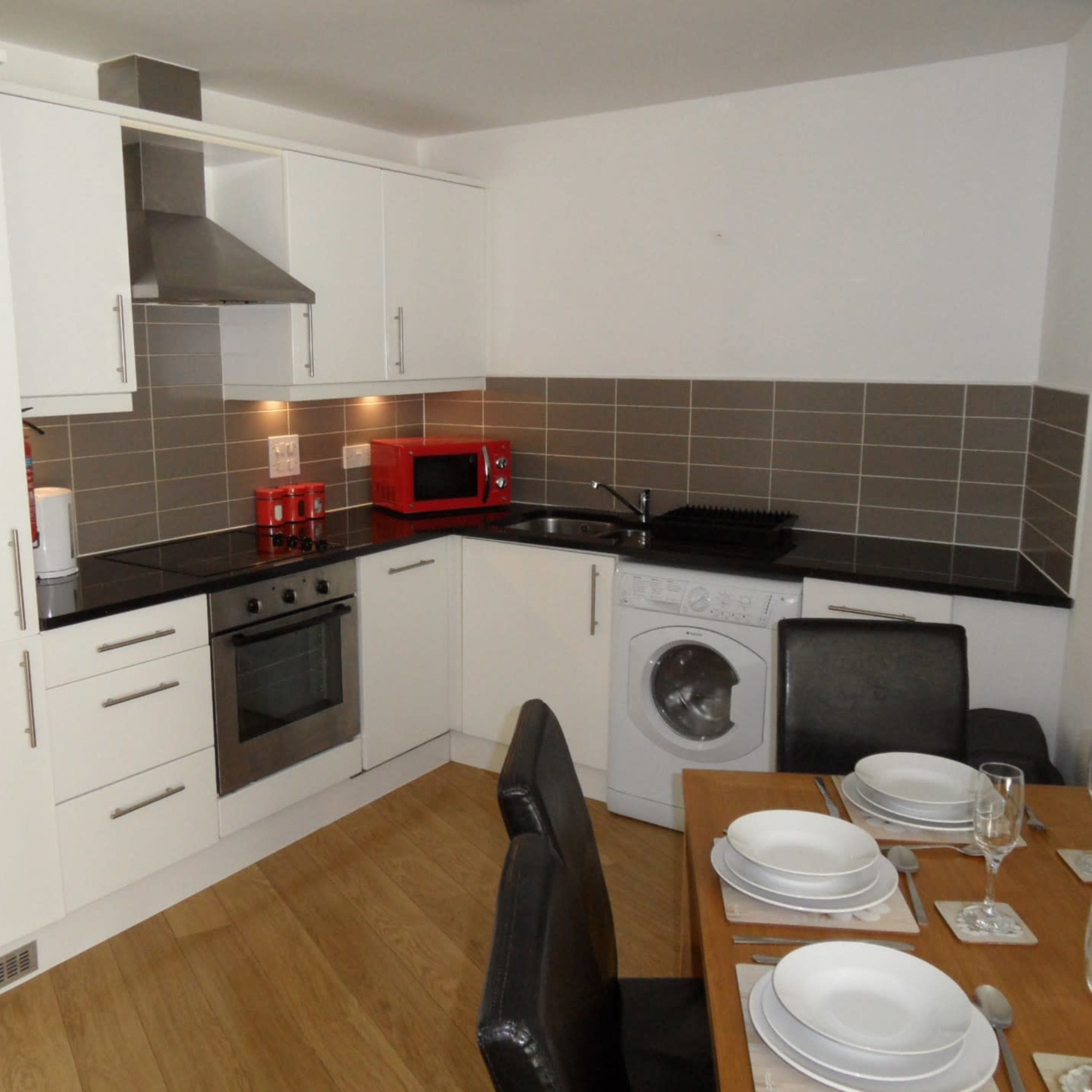A modern kitchen with white cabinets, stainless steel appliances, and a wooden dining table set with plates and glasses.