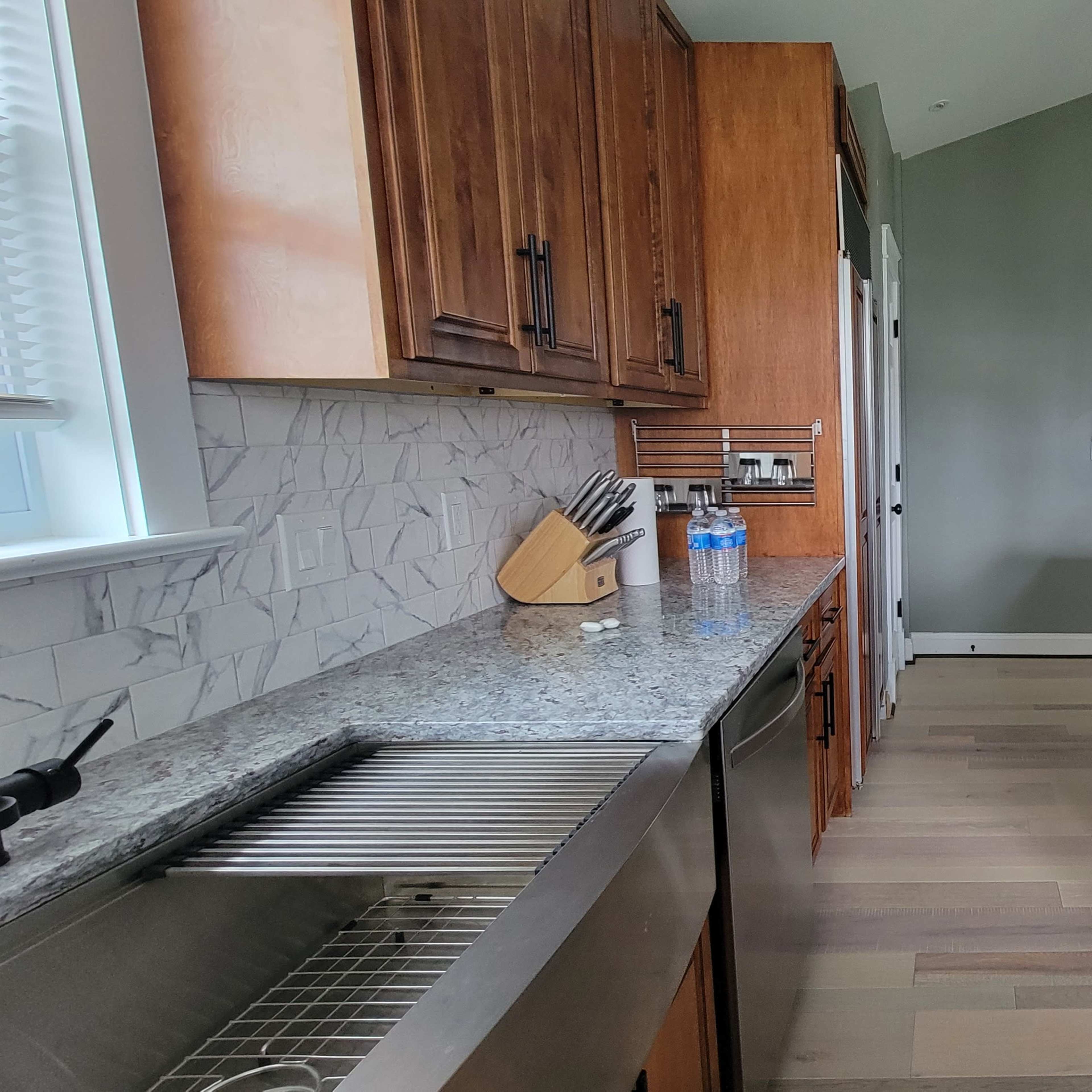 A modern kitchen features wooden cabinetry, a granite countertop, and stainless steel appliances, with a view into an adjoining room.