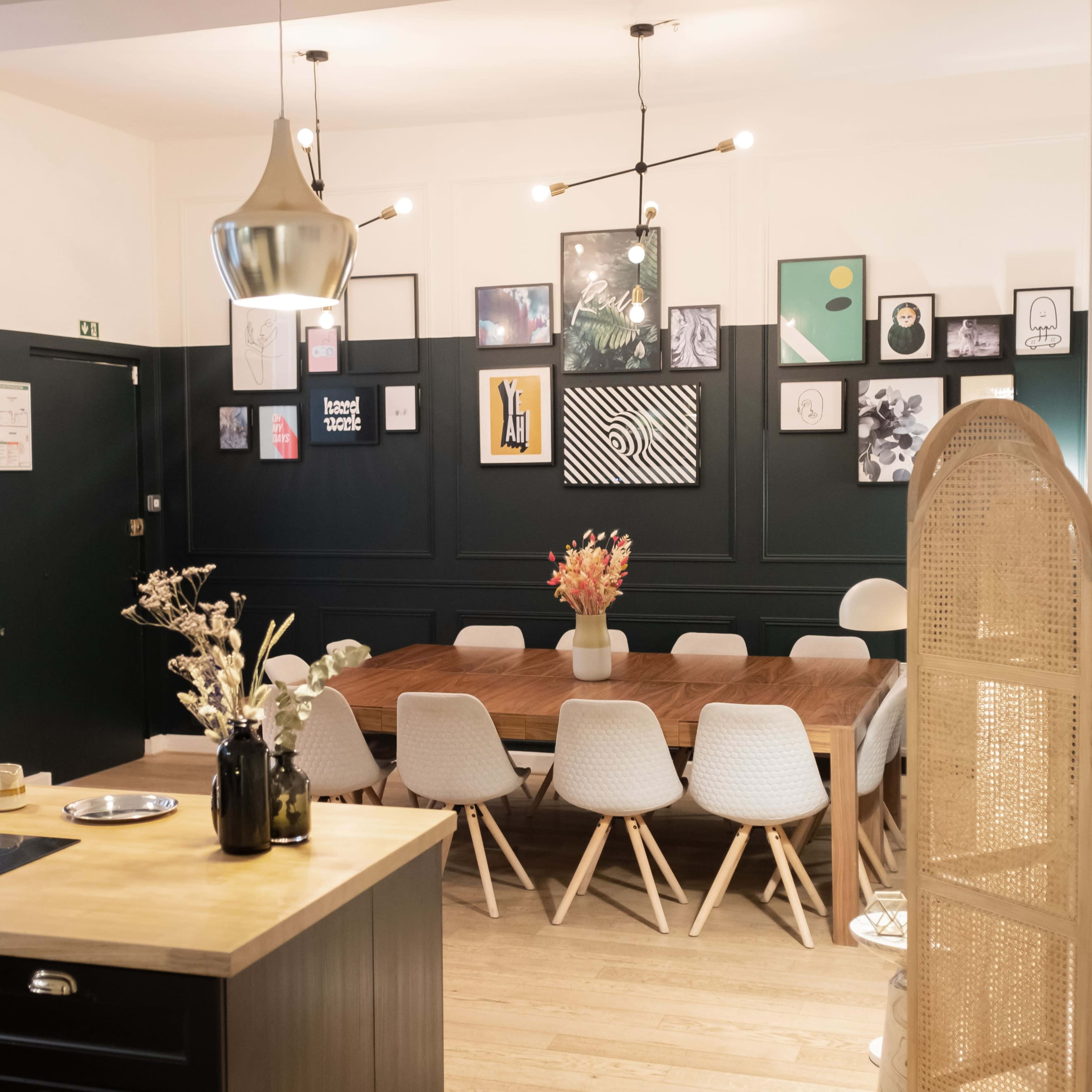 A modern dining area features a wooden table surrounded by white chairs, with a gallery wall of framed art and stylish pendant lights overhead.