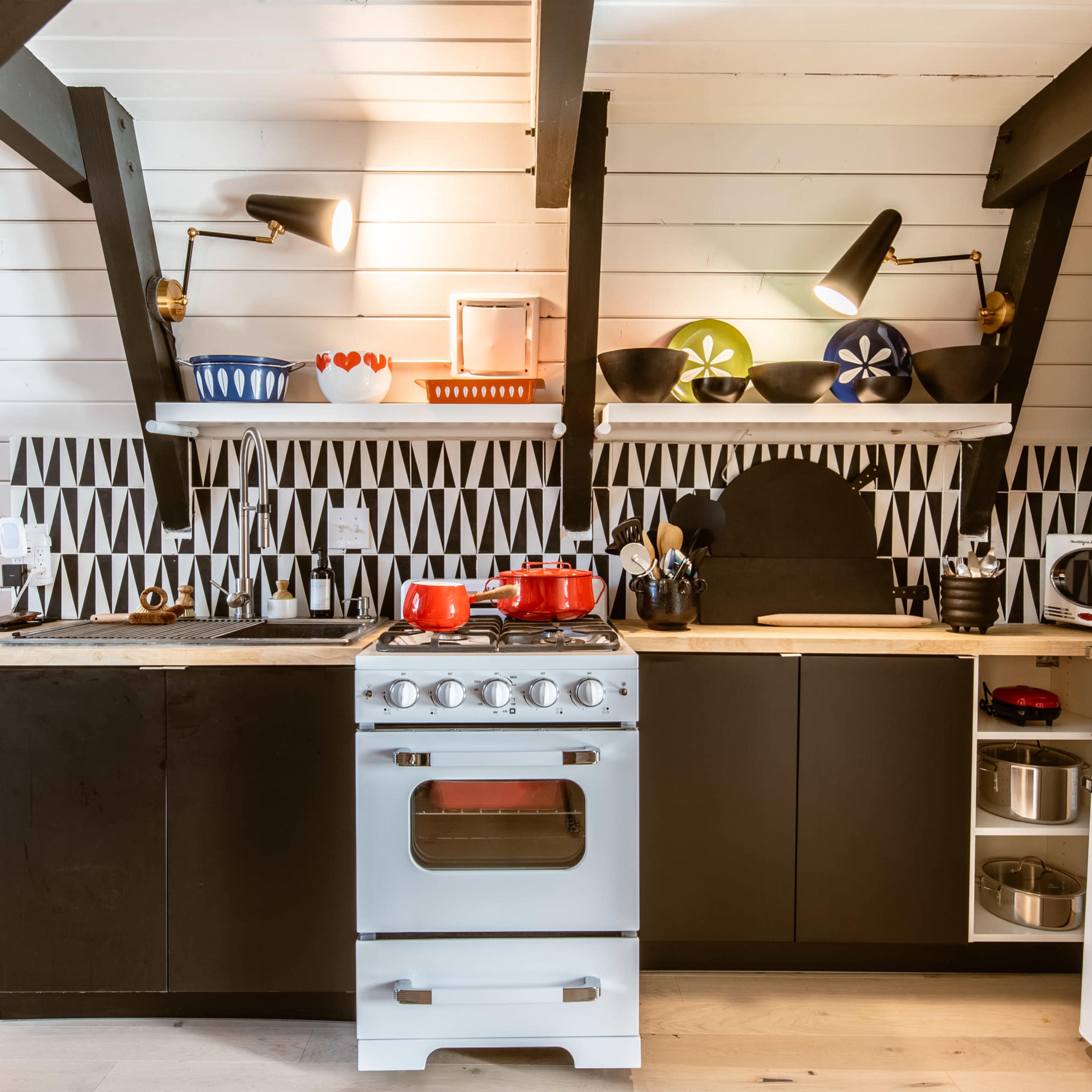 A modern kitchen with black cabinetry, an industrial stove, and decorative ceramic dishes arranged on open shelves.