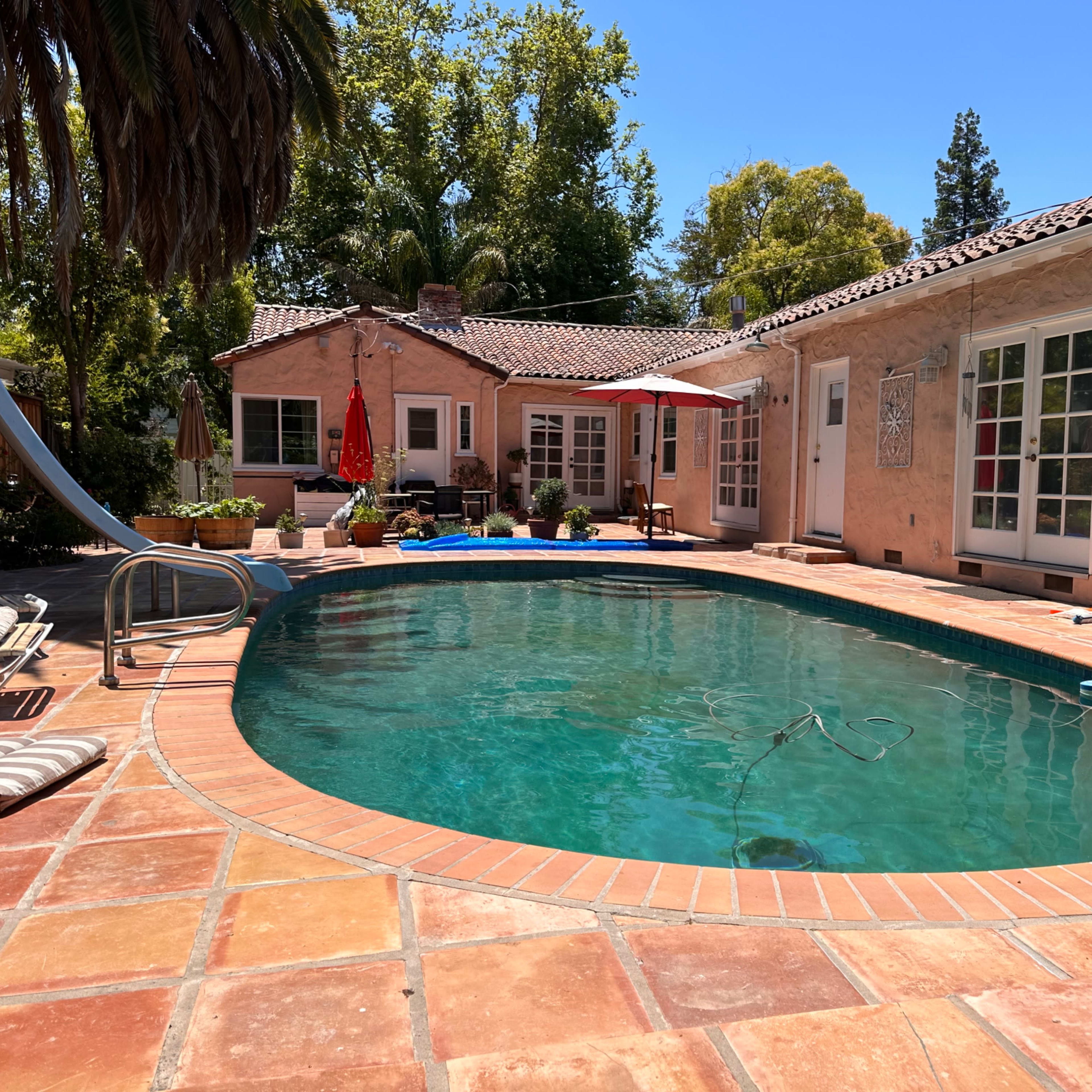 A private pool surrounded by a patio and a house with a tile roof and sliding glass doors.