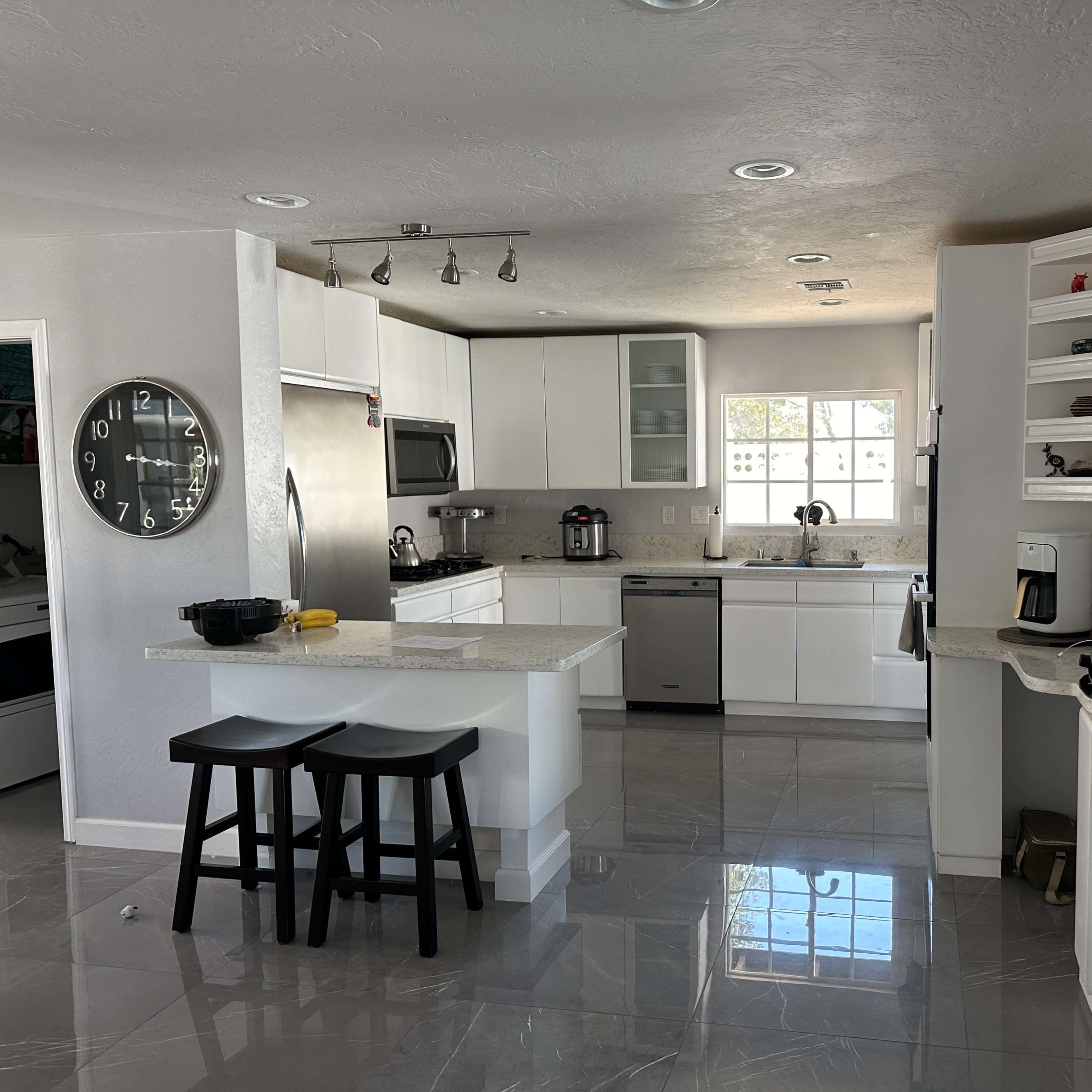 A modern kitchen with an island, stainless steel appliances, white cabinets, and gray tile flooring.