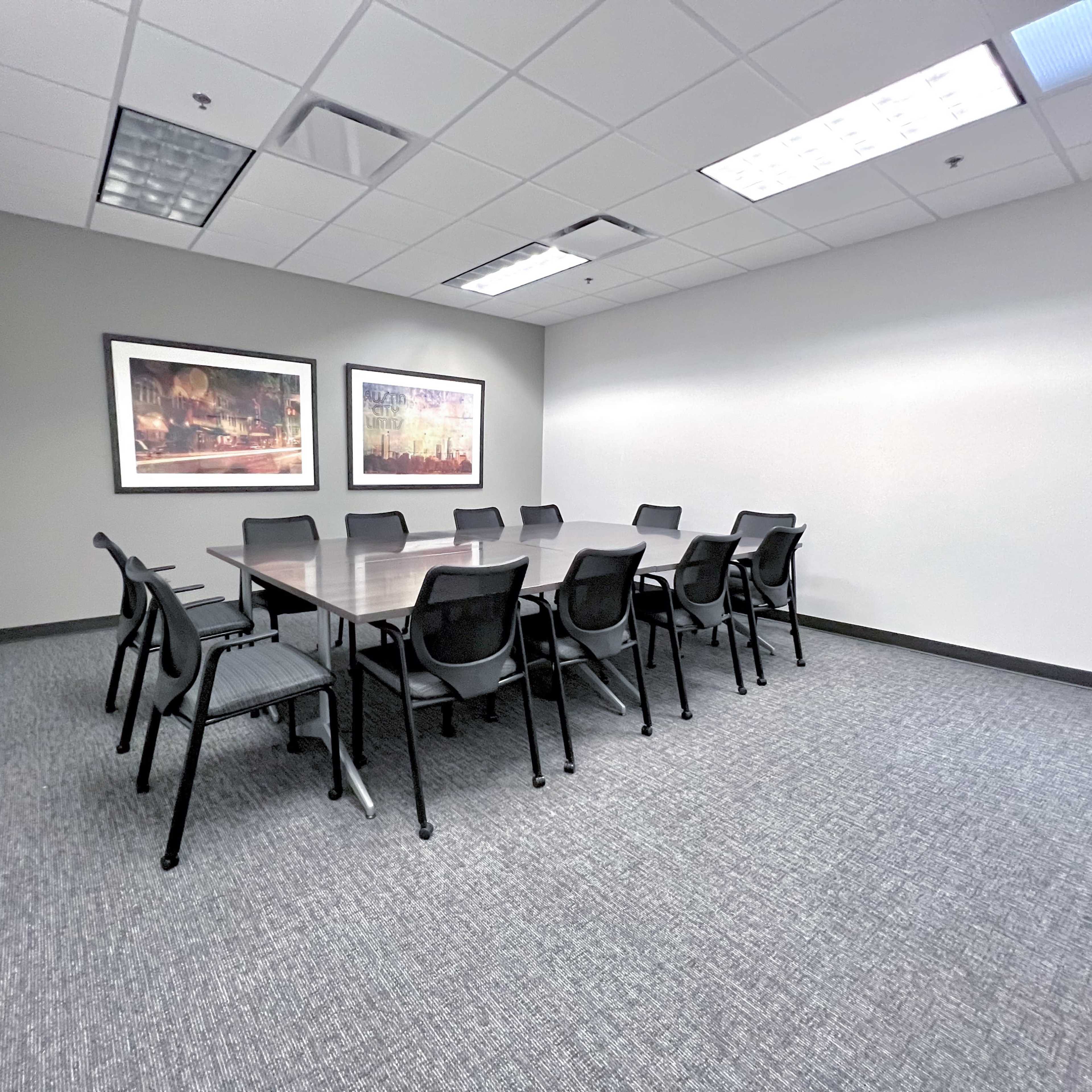 A large conference room with a rectangular table surrounded by twelve chairs and two framed artworks on the walls.