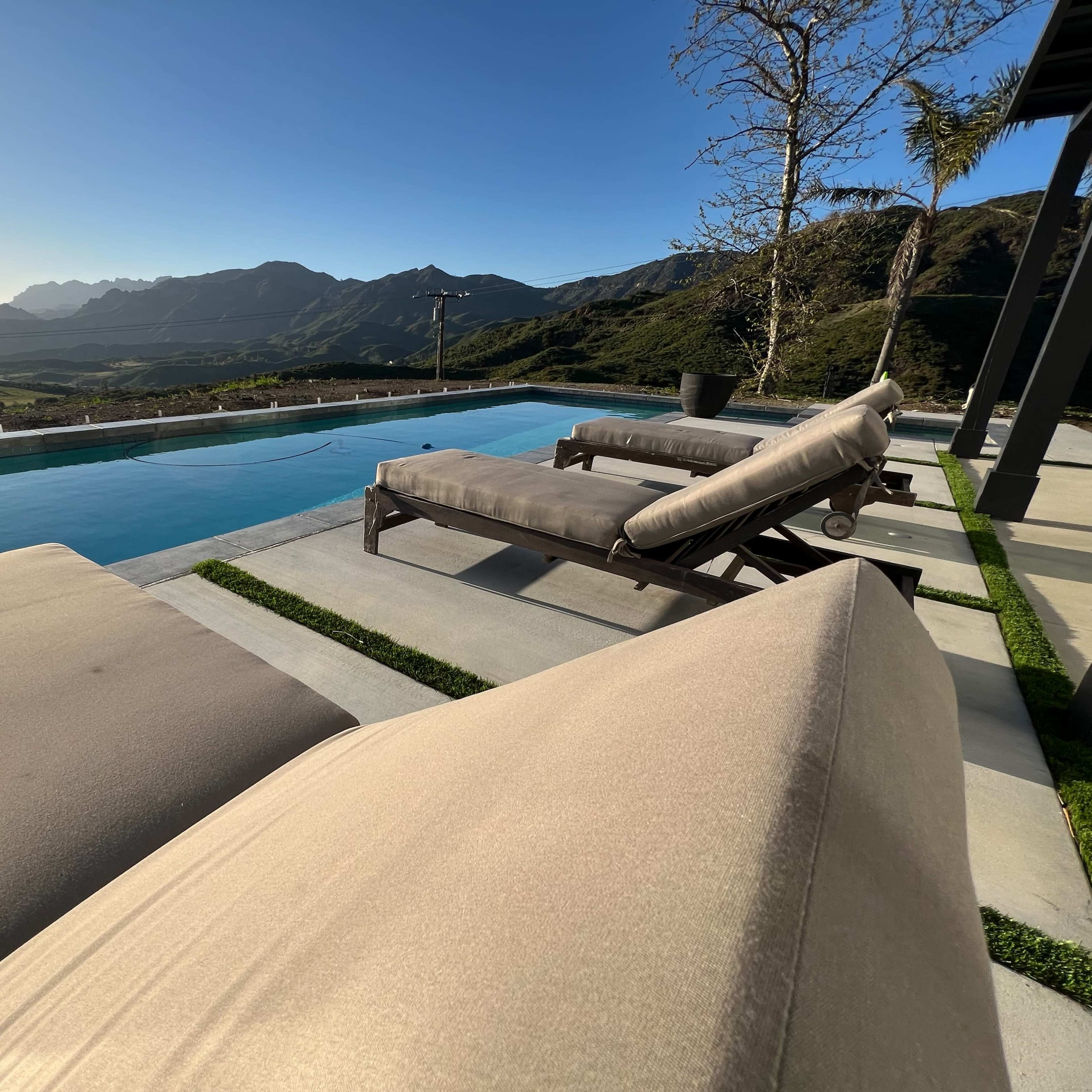 A poolside view features two lounge chairs overlooking a landscape of mountains and clear sky.