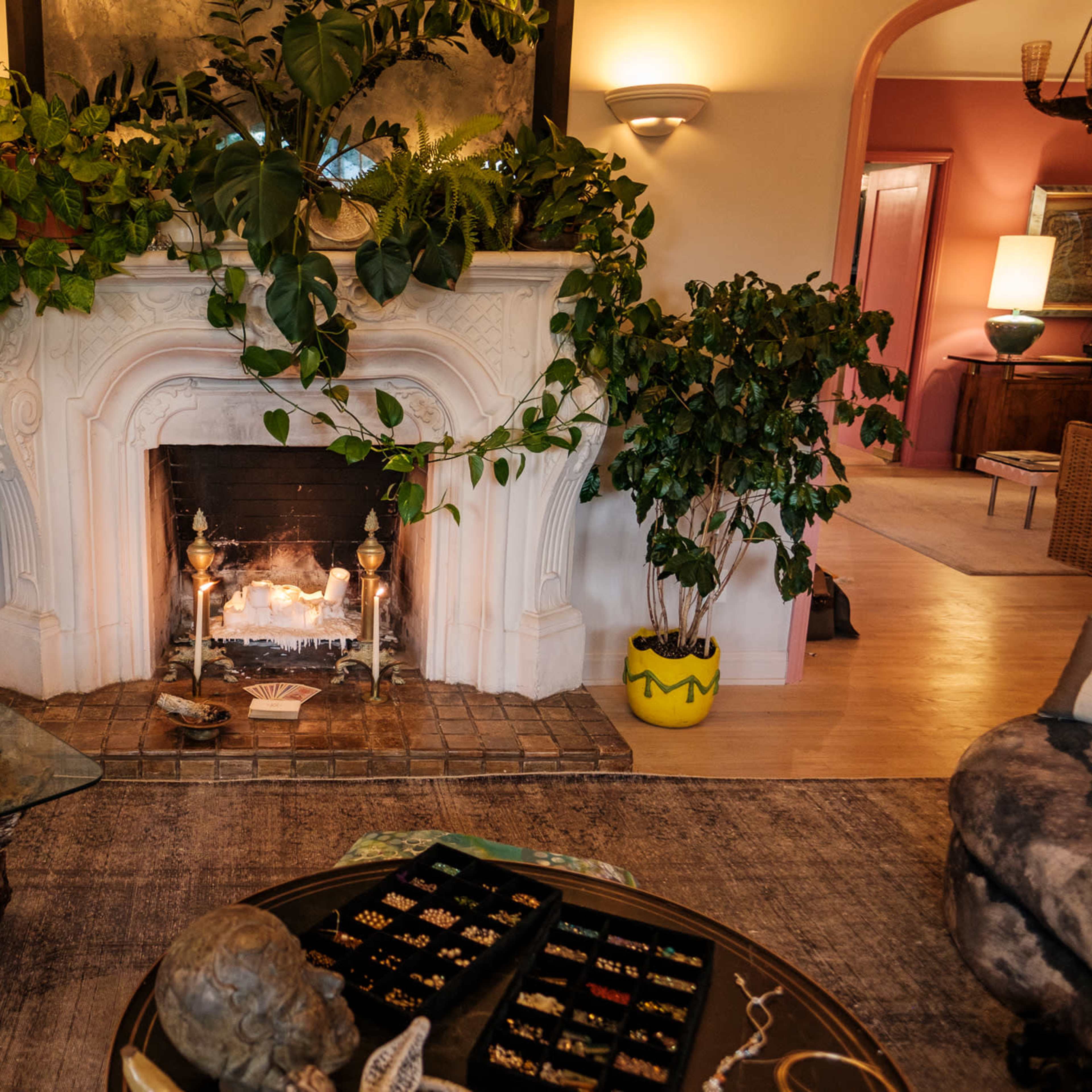A cozy living room features a fireplace adorned with greenery and a coffee table displaying various jewelry pieces.