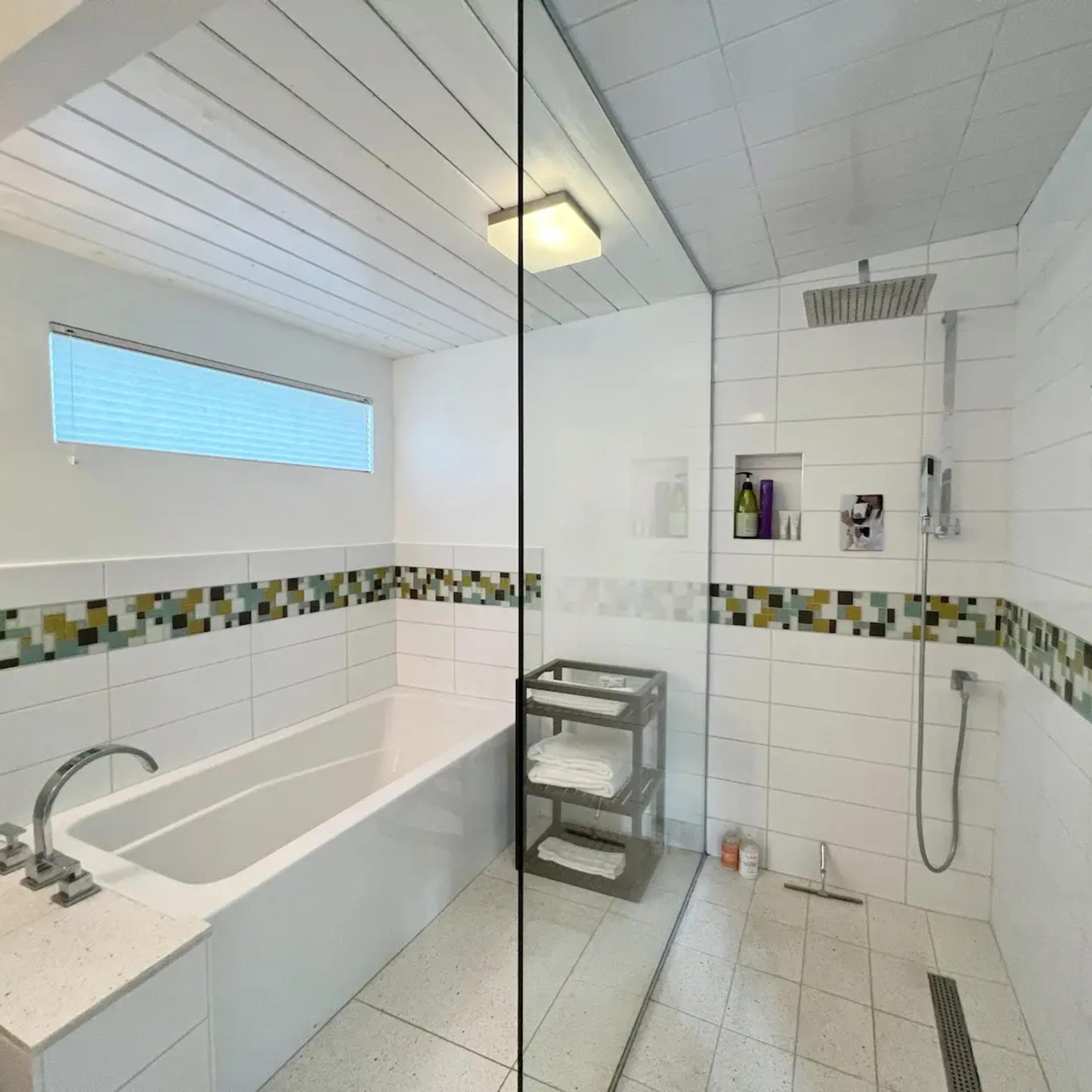 A modern bathroom with a glass shower enclosure, a bathtub, and tiled walls featuring a colored strip.