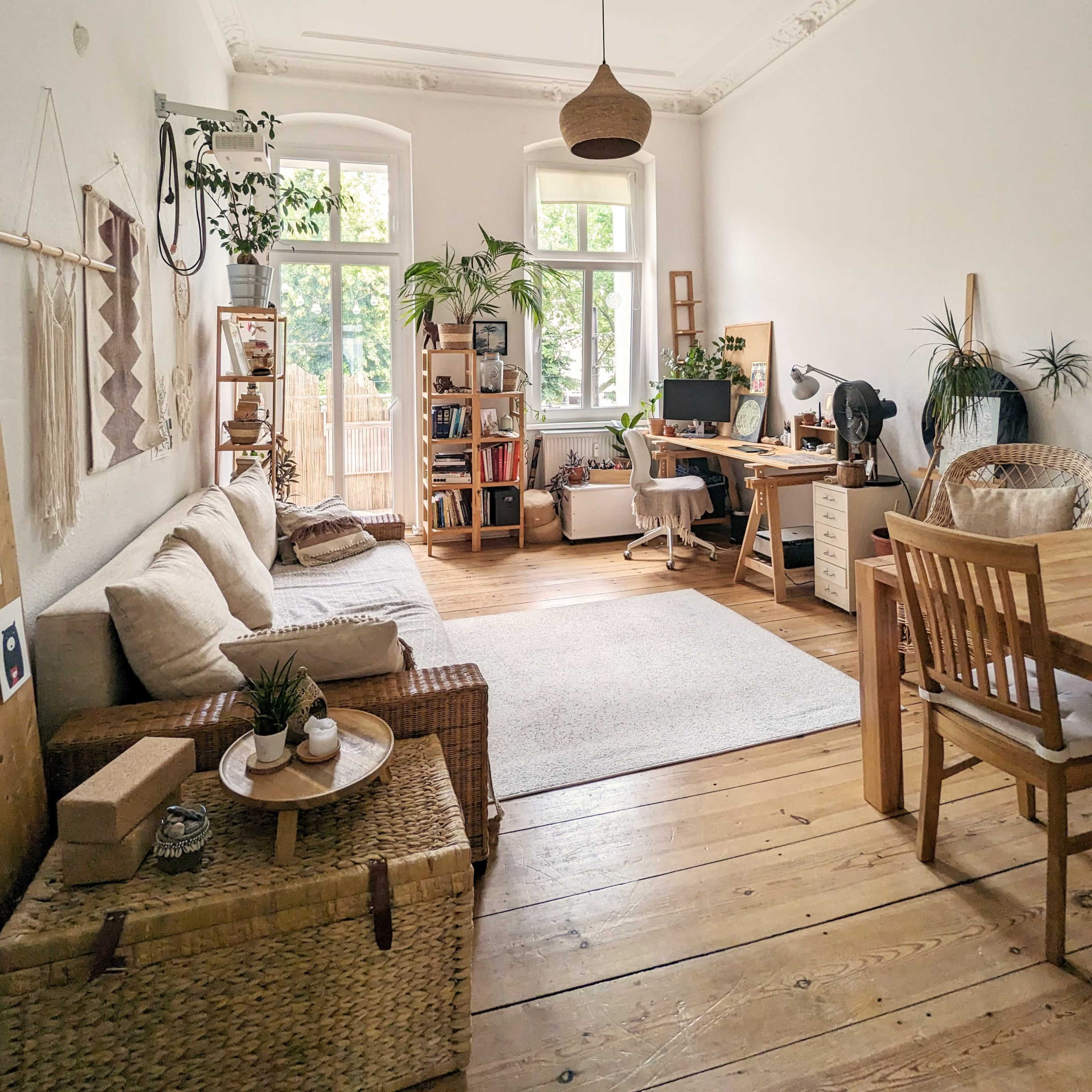 A bright, airy living space featuring a cozy seating area, a desk, plants, and wooden furniture.