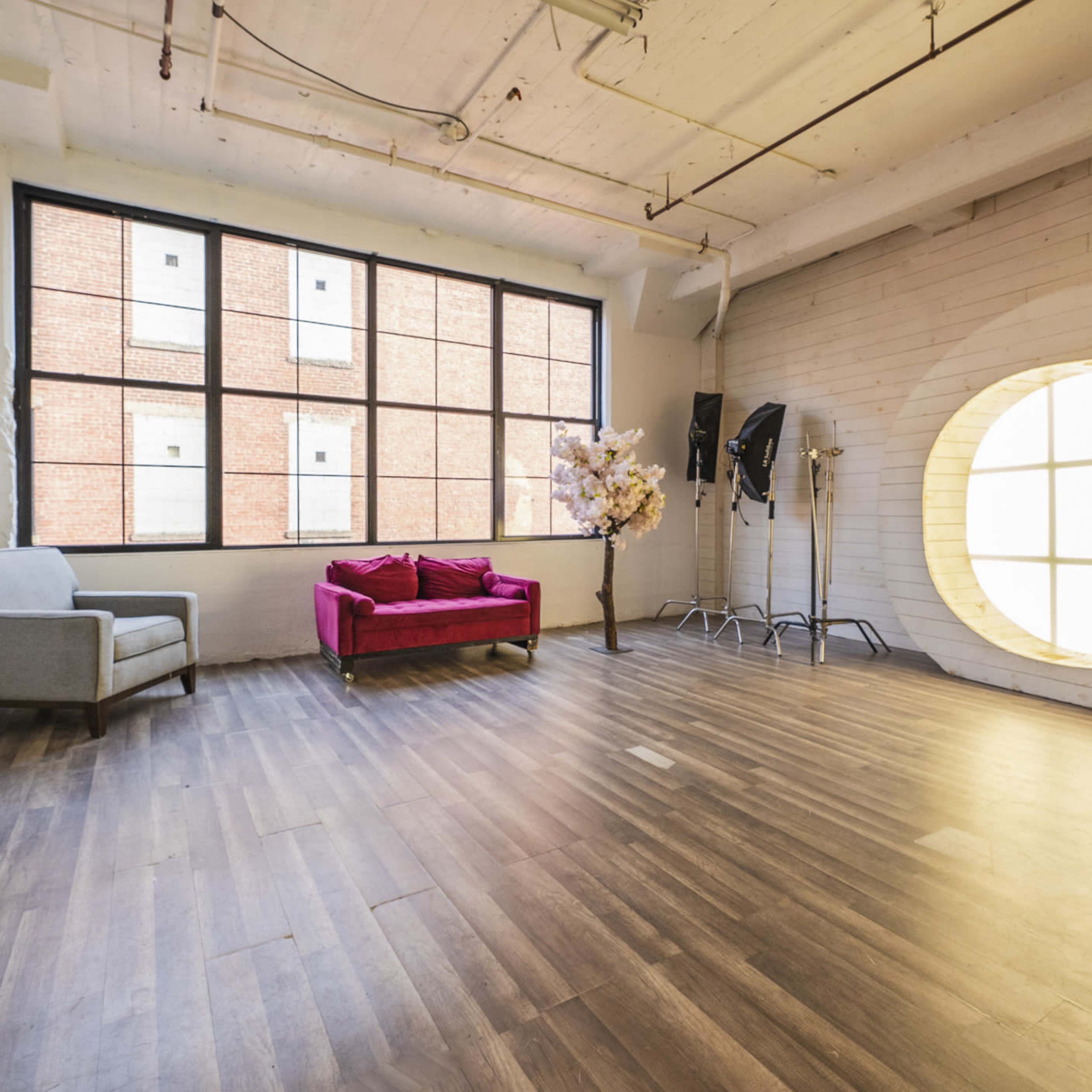 A spacious room with large windows, a pink sofa, and a round, wooden installation on one wall.