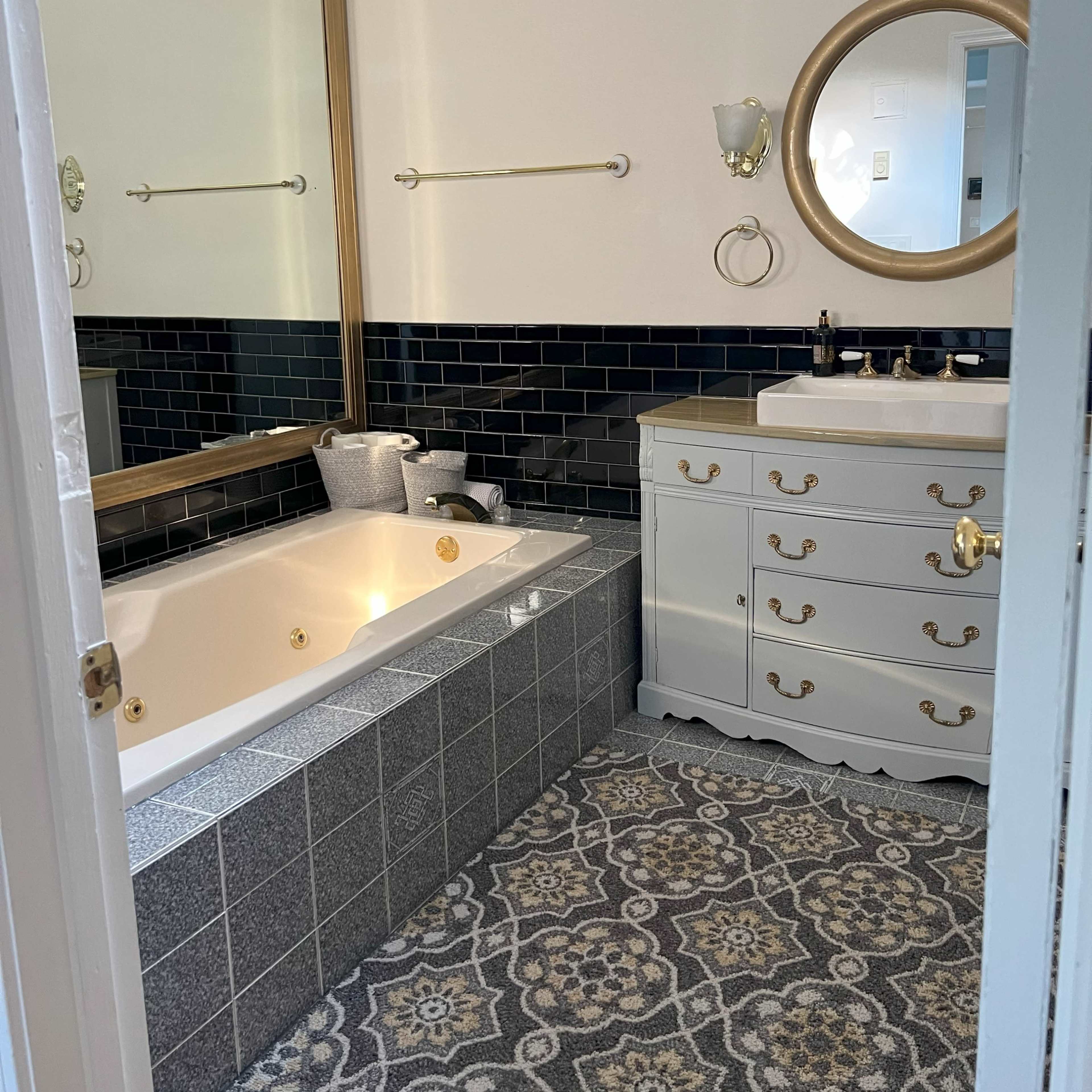 A bathroom features a jetted tub, a double sink vanity, and a patterned tile floor, with a large mirror reflecting the space.