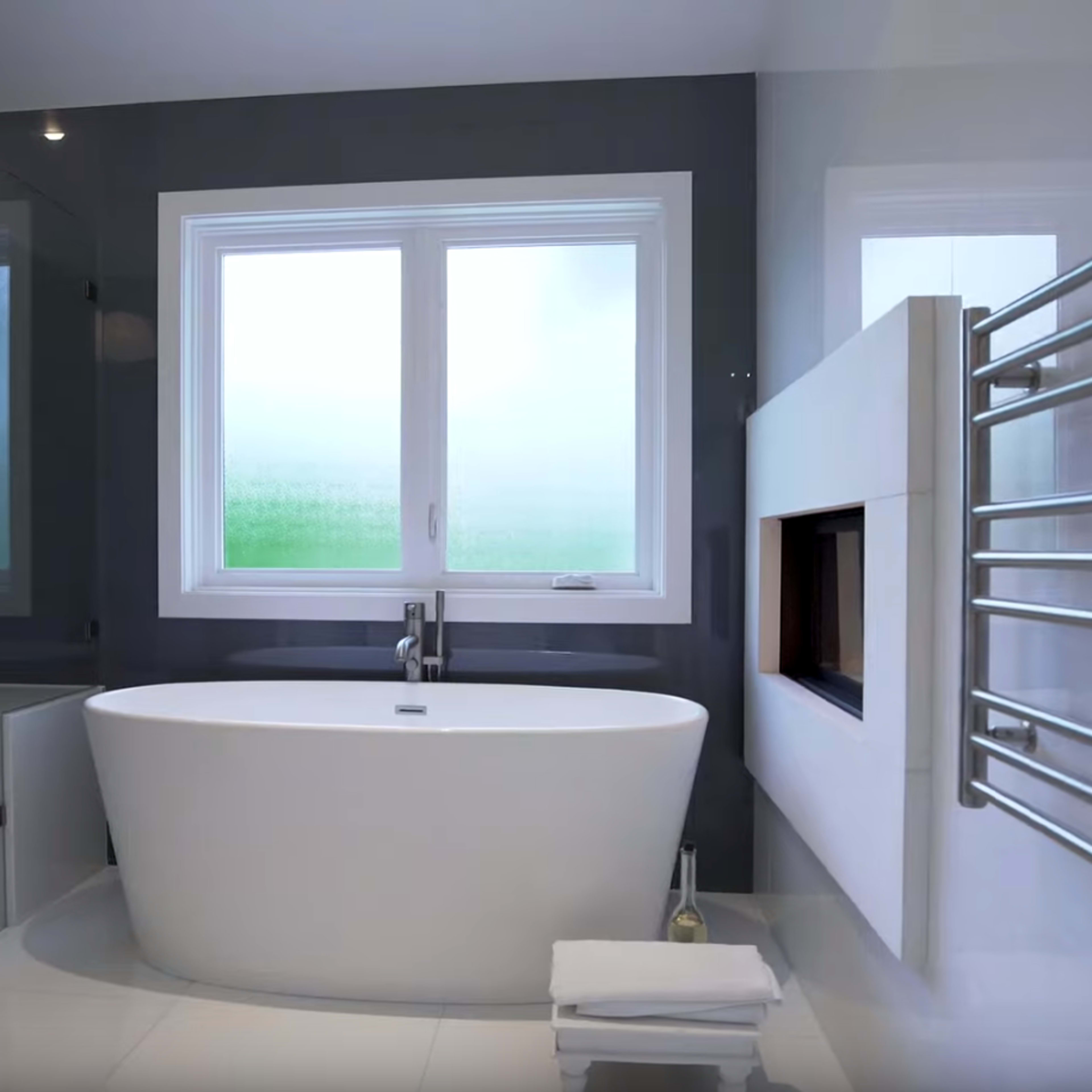 The bathroom features a freestanding bathtub, a glass shower enclosure, and a sleek heating towel rail against a grey wall.
