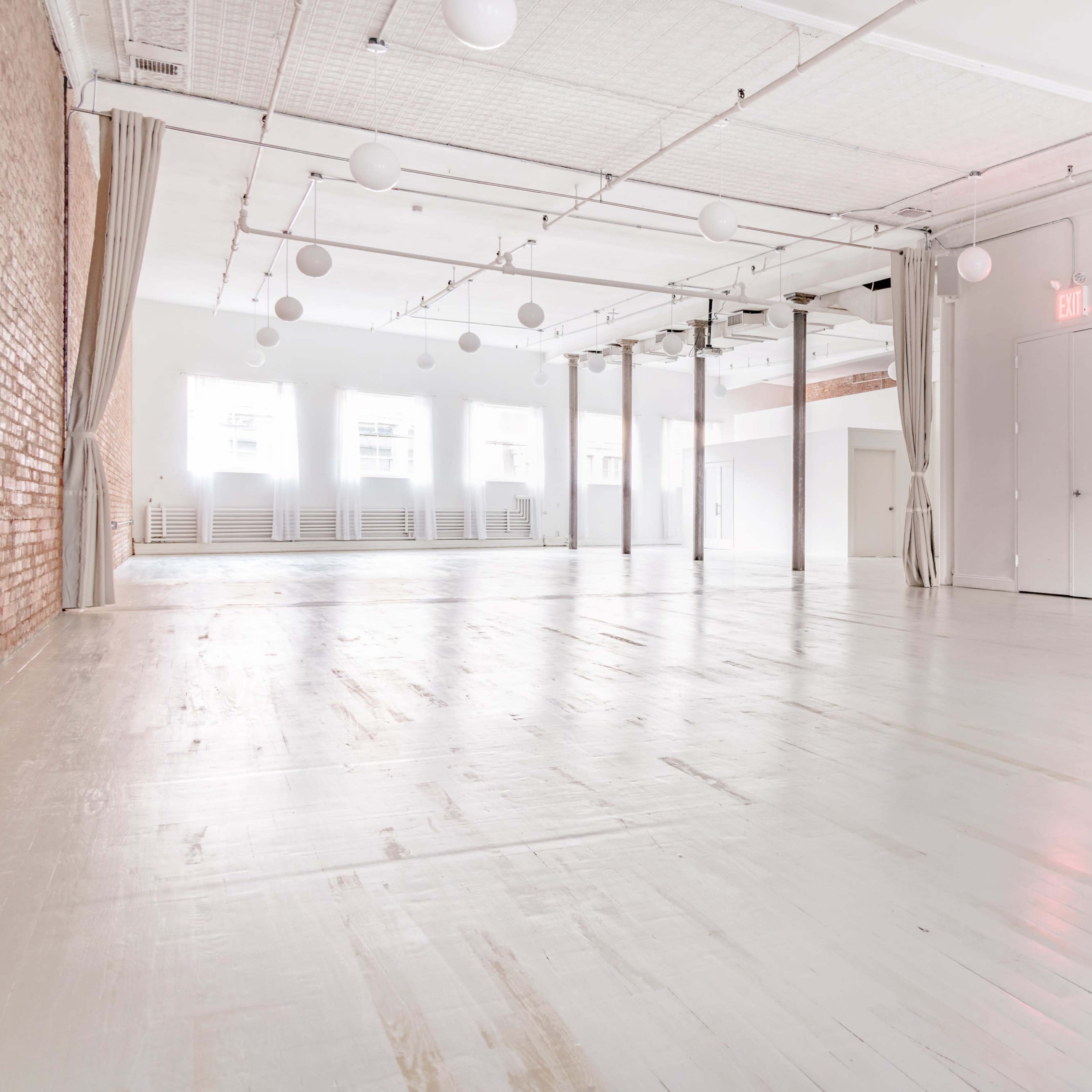 A spacious white interior room with wooden floors, large windows, and pendant lighting.