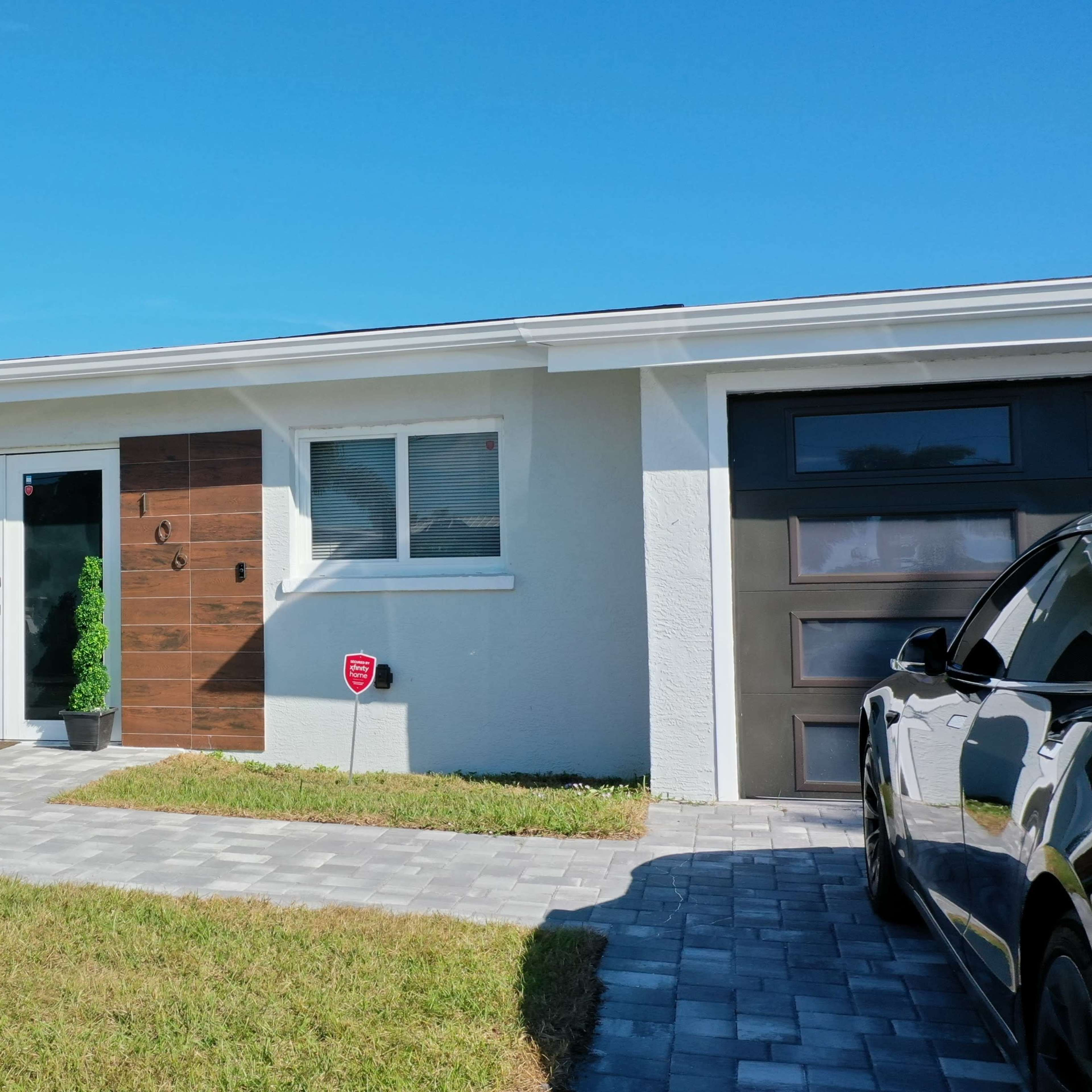 A modern house with a light-colored exterior, a wooden accent wall, and landscaped grass in the front yard.