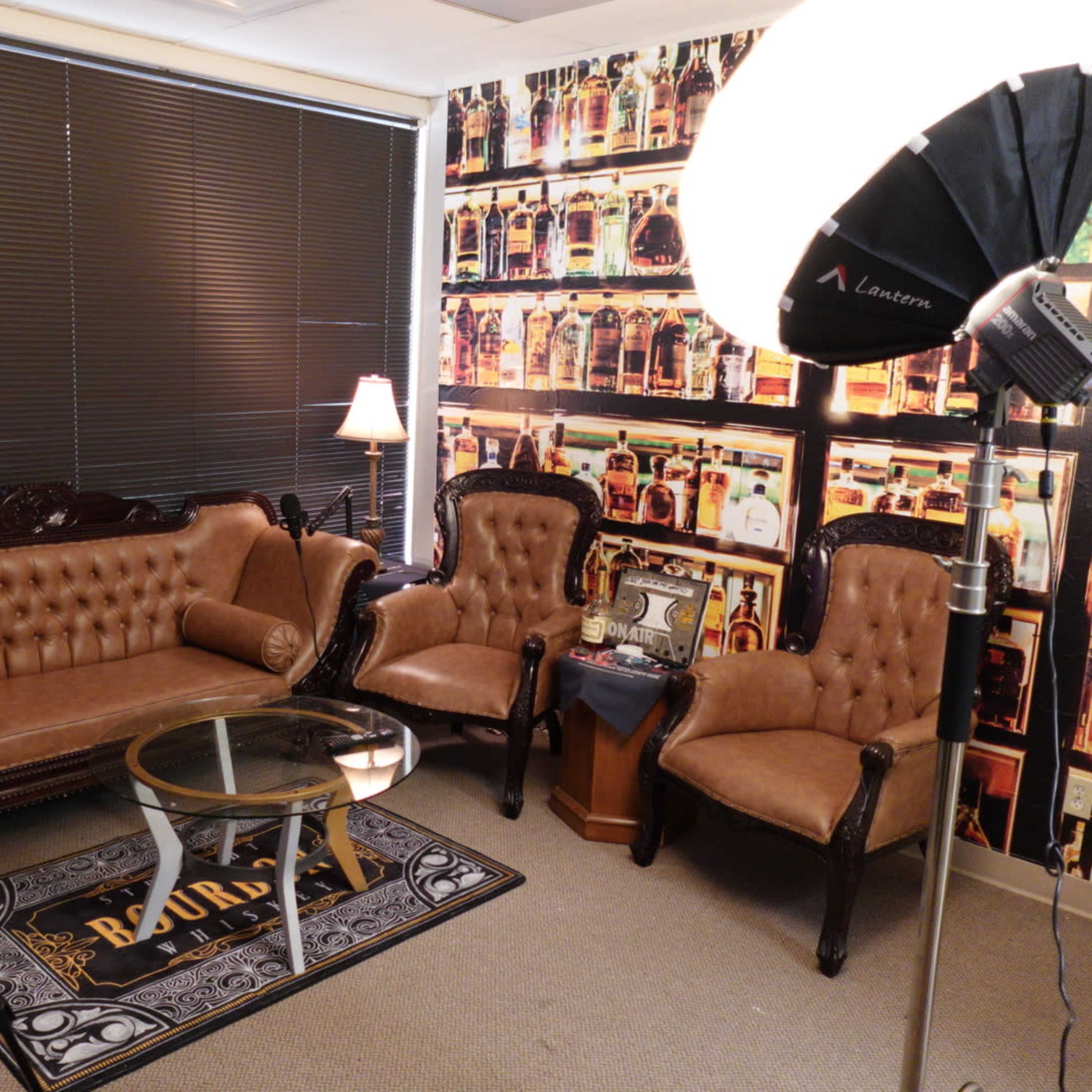 A small sitting area with tufted leather sofas, a glass coffee table, and a backdrop of a patterned wallpaper featuring bottles.