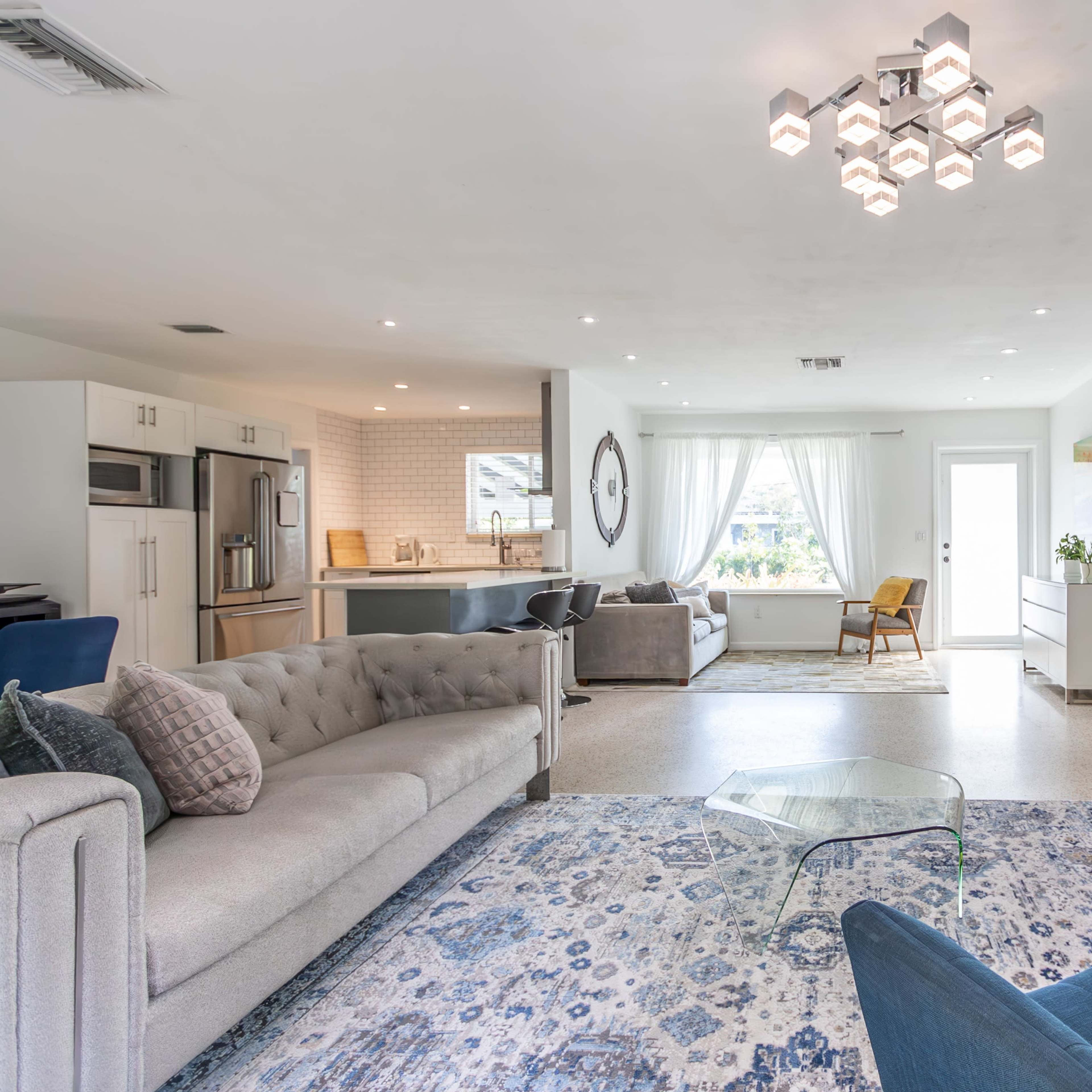 A modern living room with a sectional sofa, a glass coffee table, and a view of a kitchen area in the background.