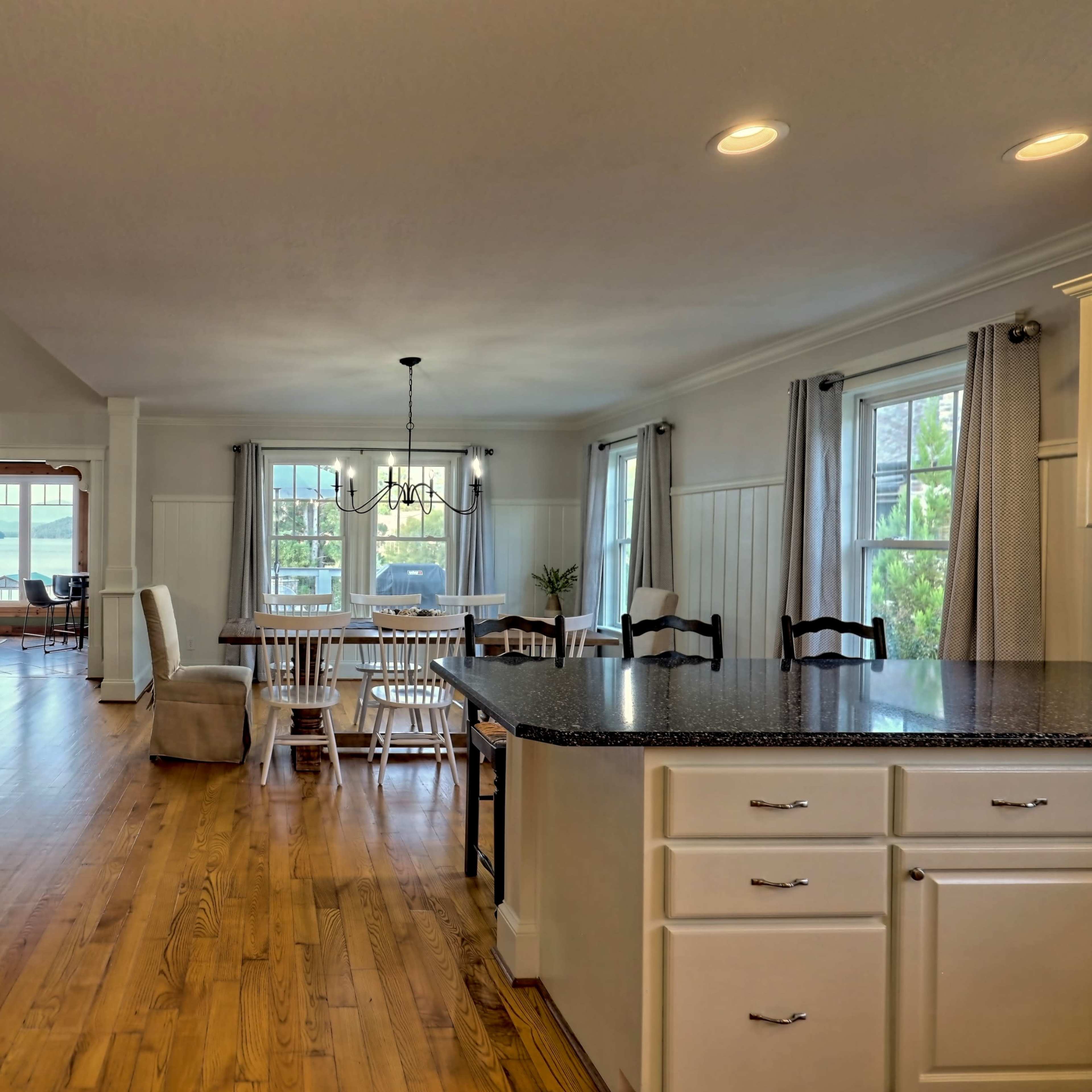 An open-concept living space featuring a kitchen with a dark countertop, a dining area with wooden tables and chairs, and a cozy sitting area in the background.