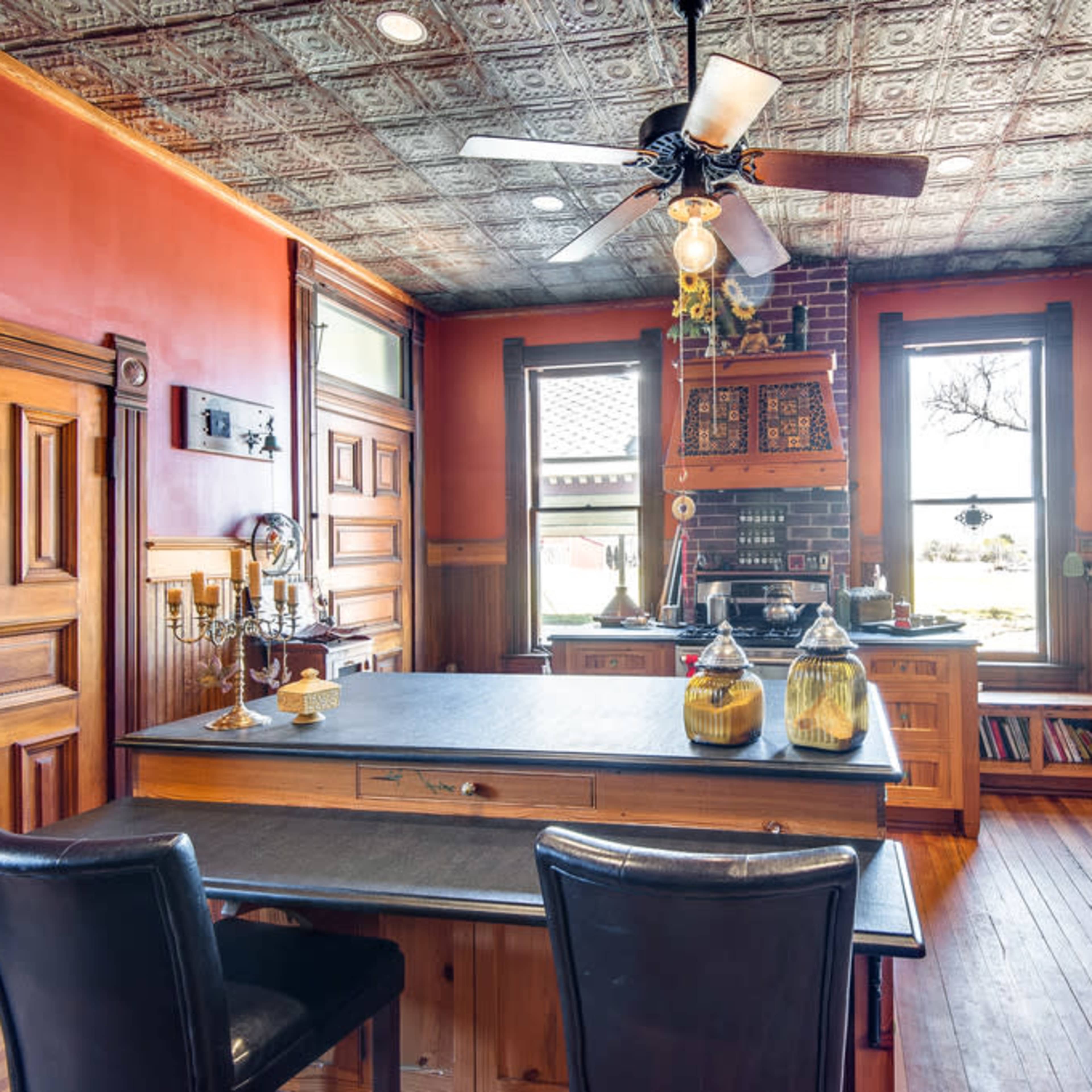 The kitchen features wooden cabinetry, a central island with a black countertop, and a ceiling adorned with decorative tin tiles.