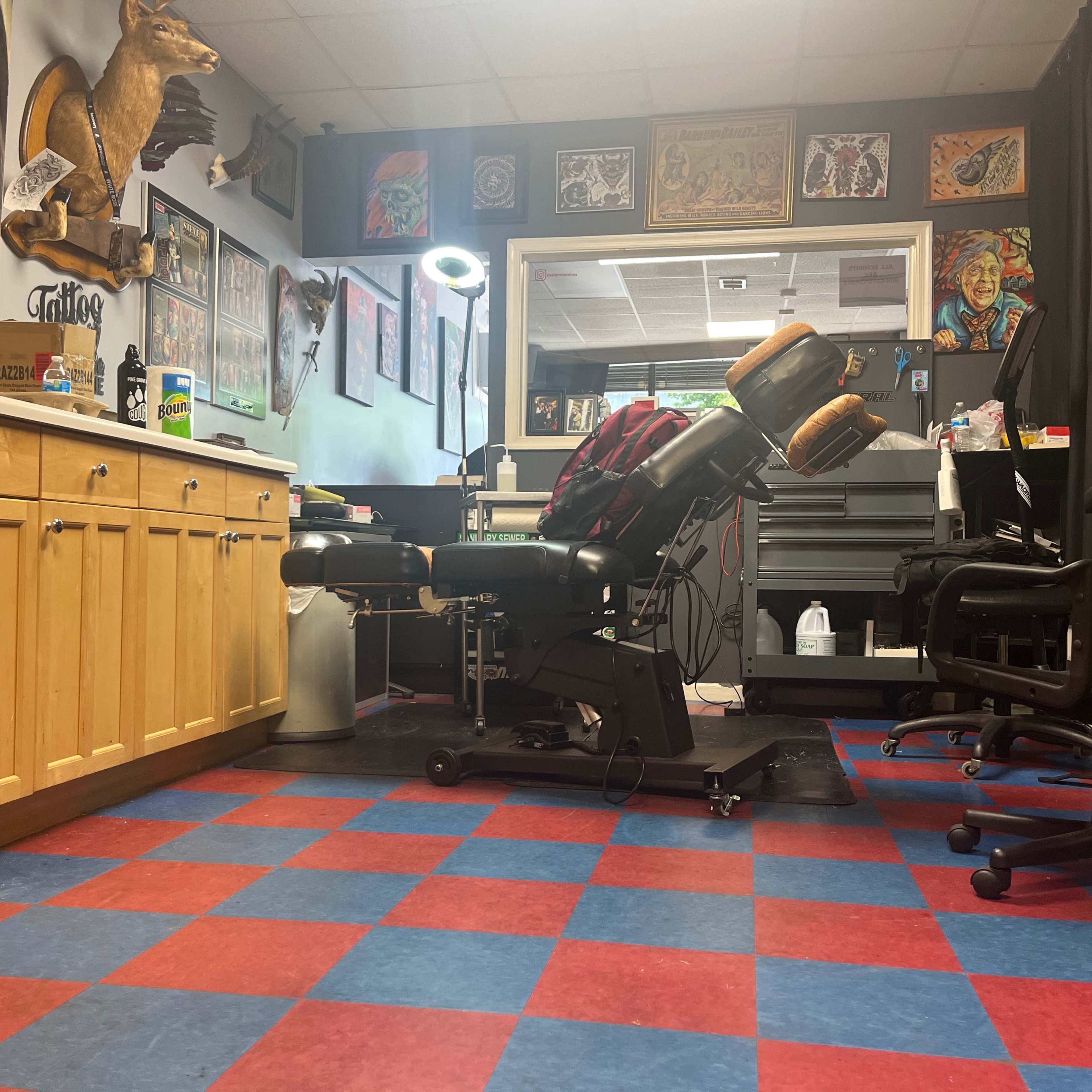 A tattoo parlor with a tattoo chair, workstations, and colorful checkered flooring.