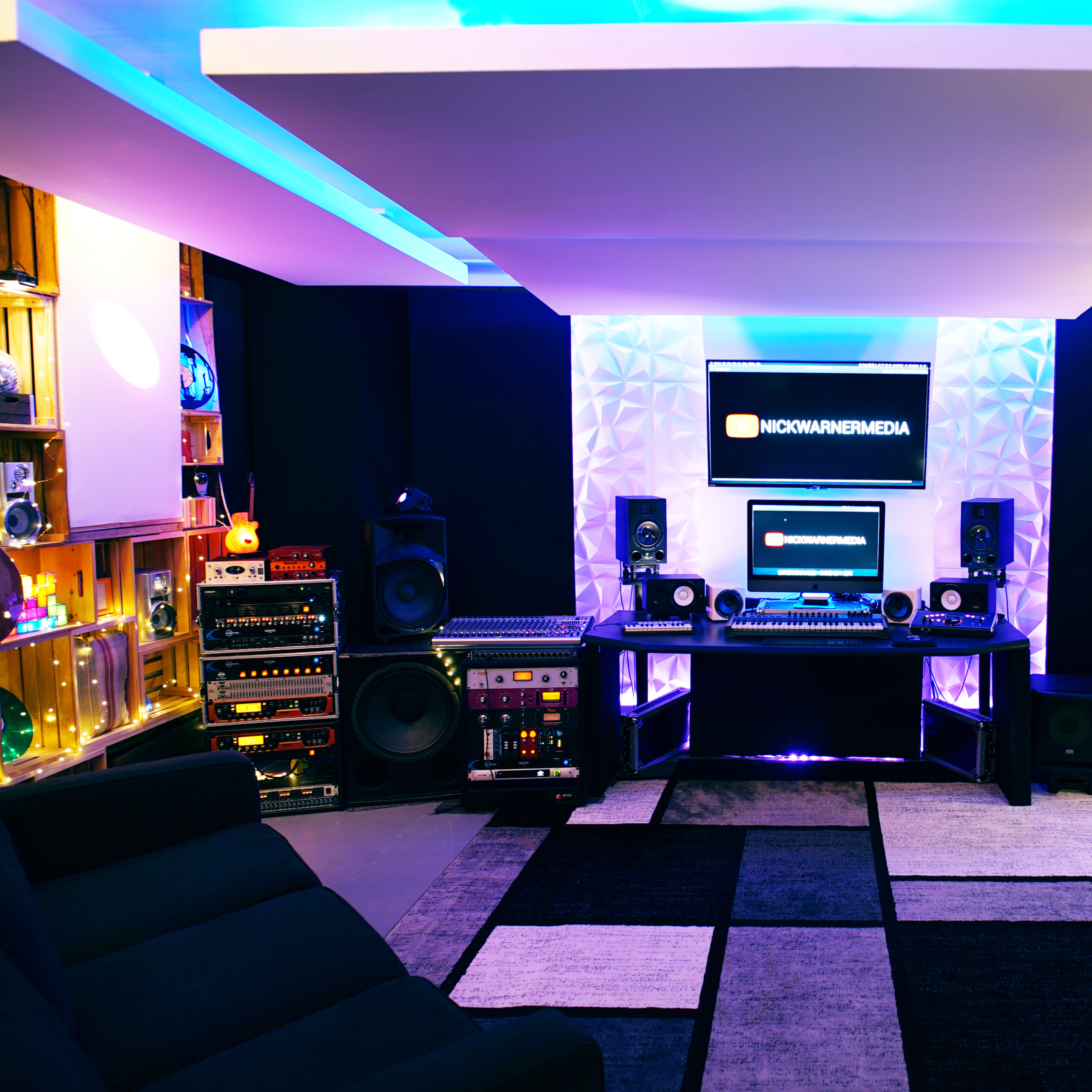 A modern recording studio features a central desk with audio equipment, surrounded by speakers and guitars, bathed in blue and purple lighting.