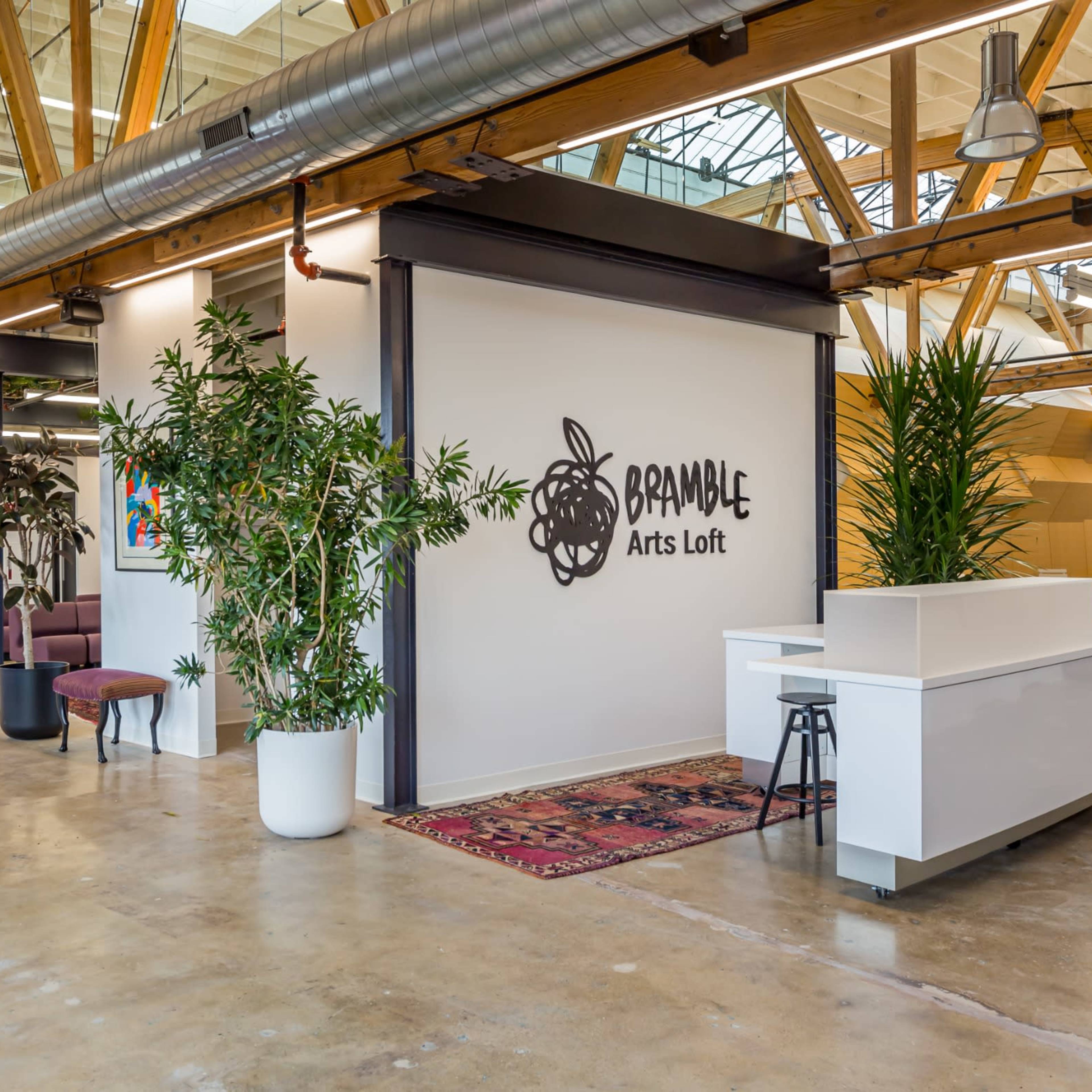 A spacious arts loft with high wooden beams, distinct areas for seating, and a reception space featuring plants and artwork against white walls.
