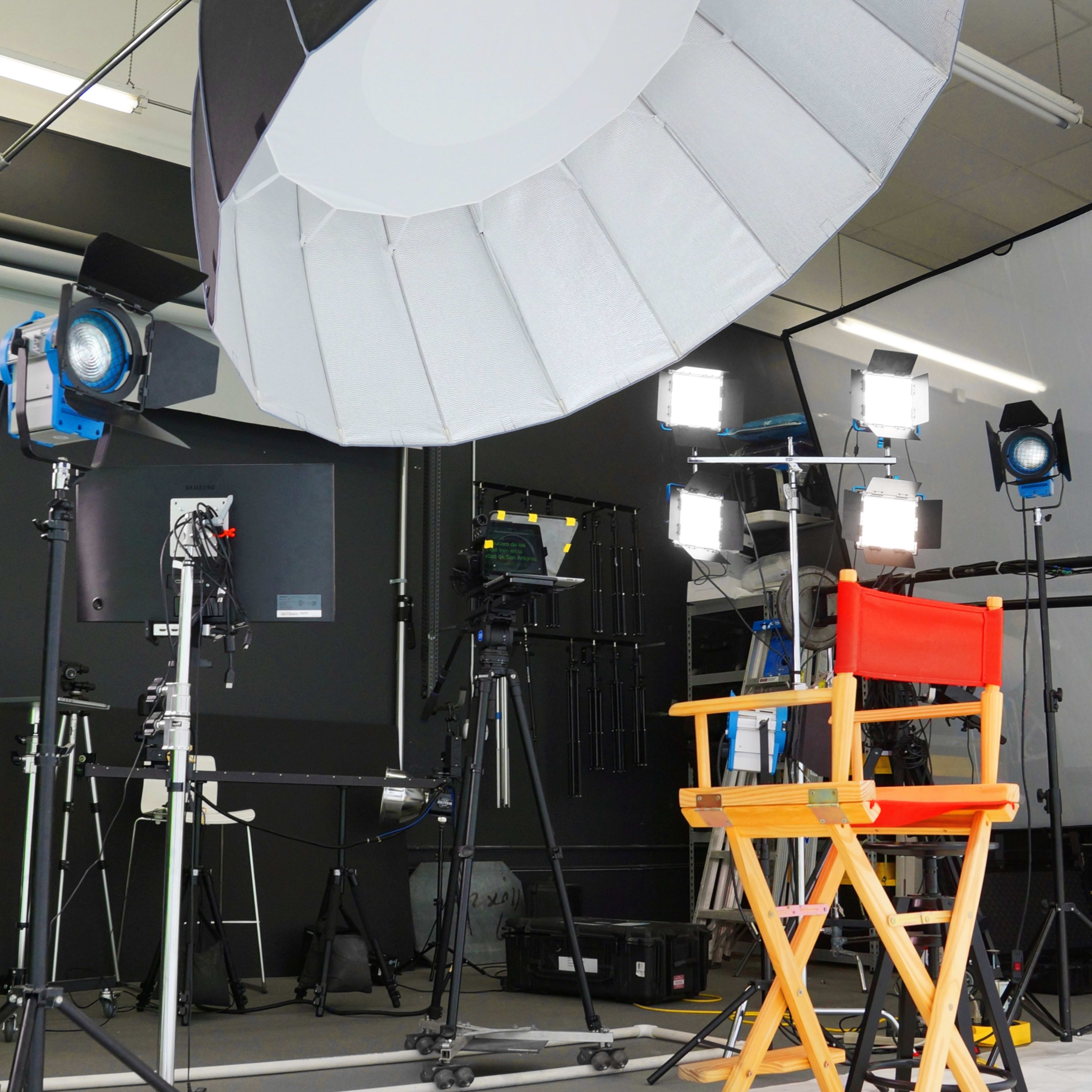 A film set with a red director's chair in front of various lighting equipment and backdrops.