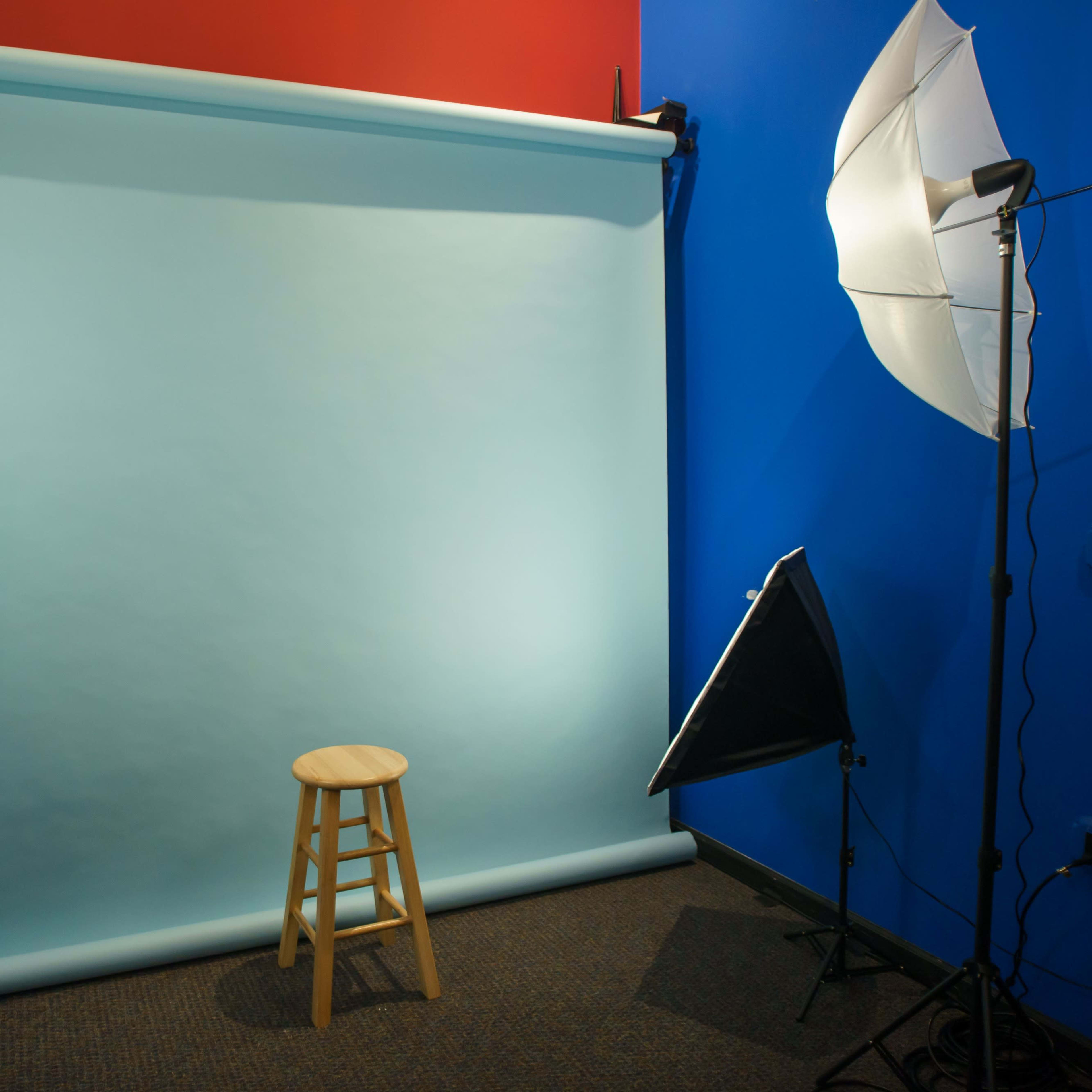 A photography setup features a blue backdrop with a wooden stool in front, flanked by softbox lights on either side.