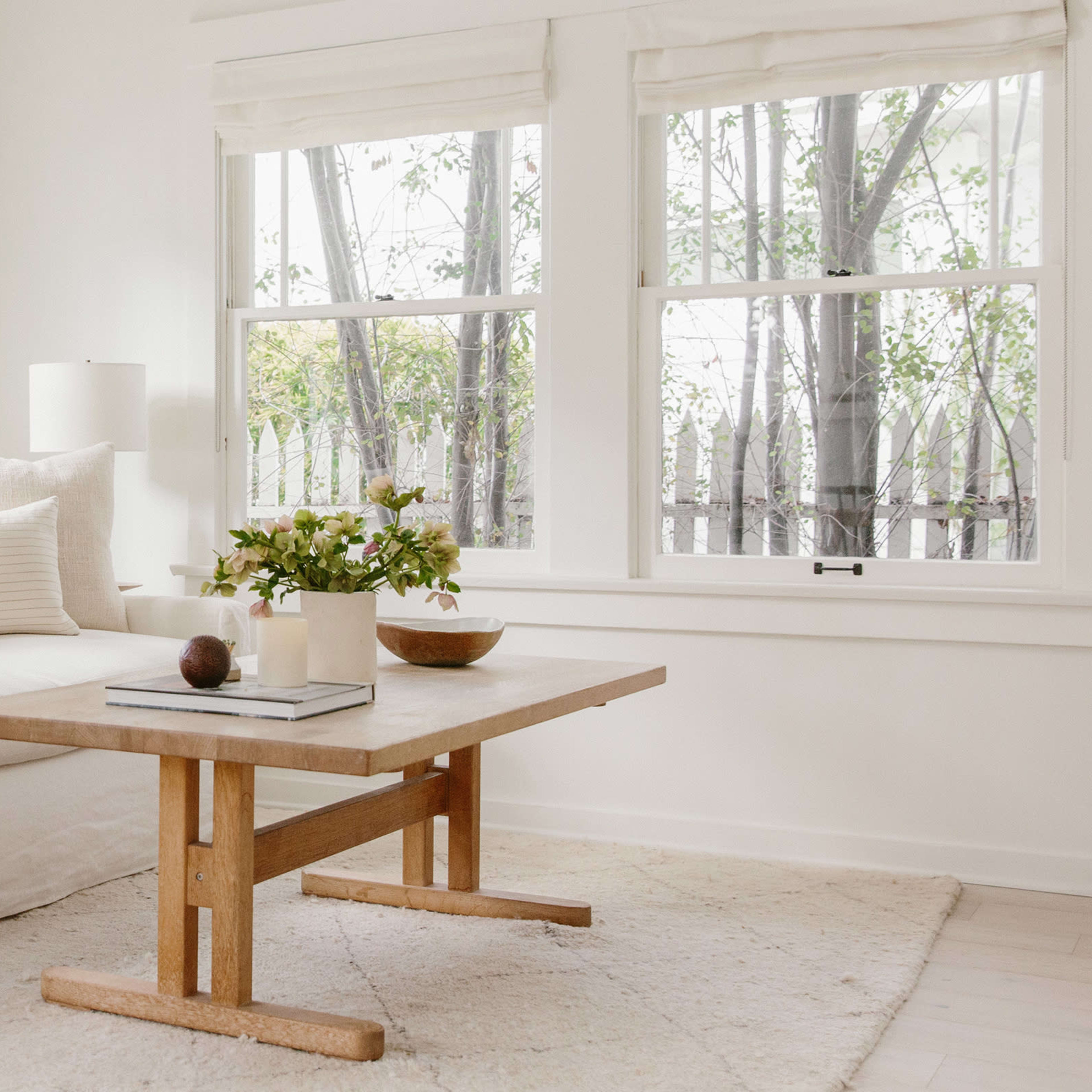 A bright living room features a white couch, a wood coffee table, and large windows letting in natural light.