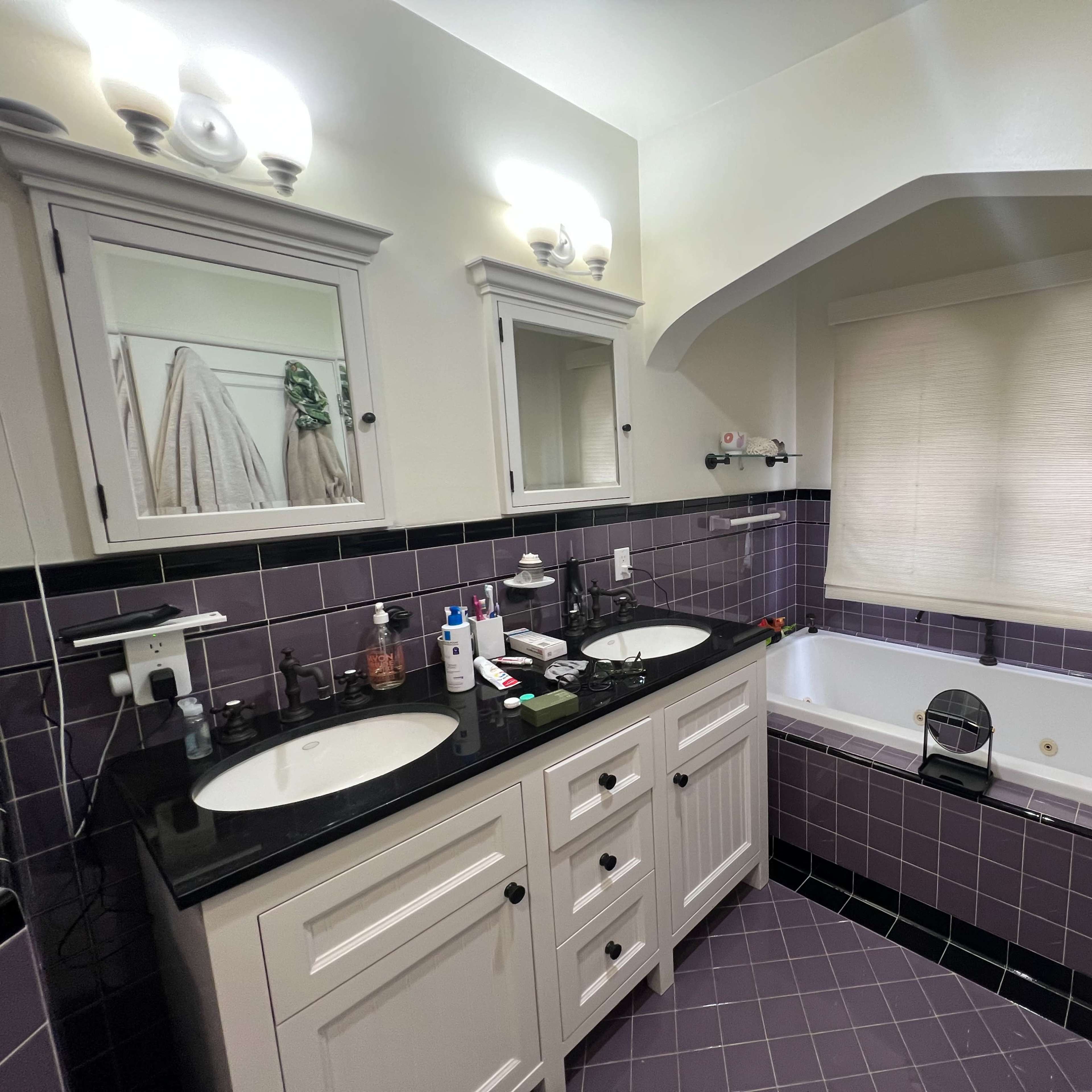 A bathroom with a double sink vanity, a bathtub, and a large window covered by a shade.