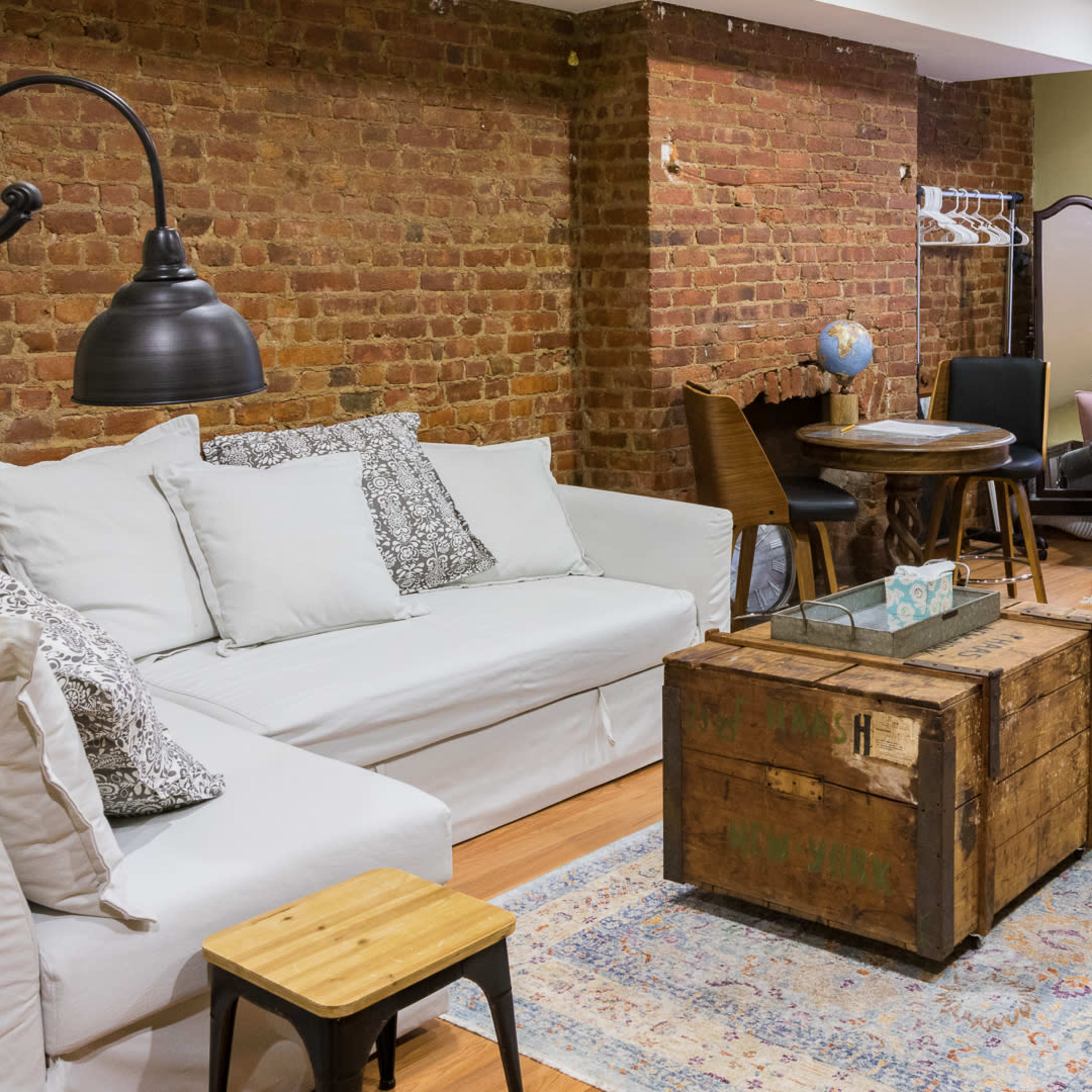 A cozy living room featuring a white sofa, a gray couch, a wooden coffee table, and exposed brick walls.
