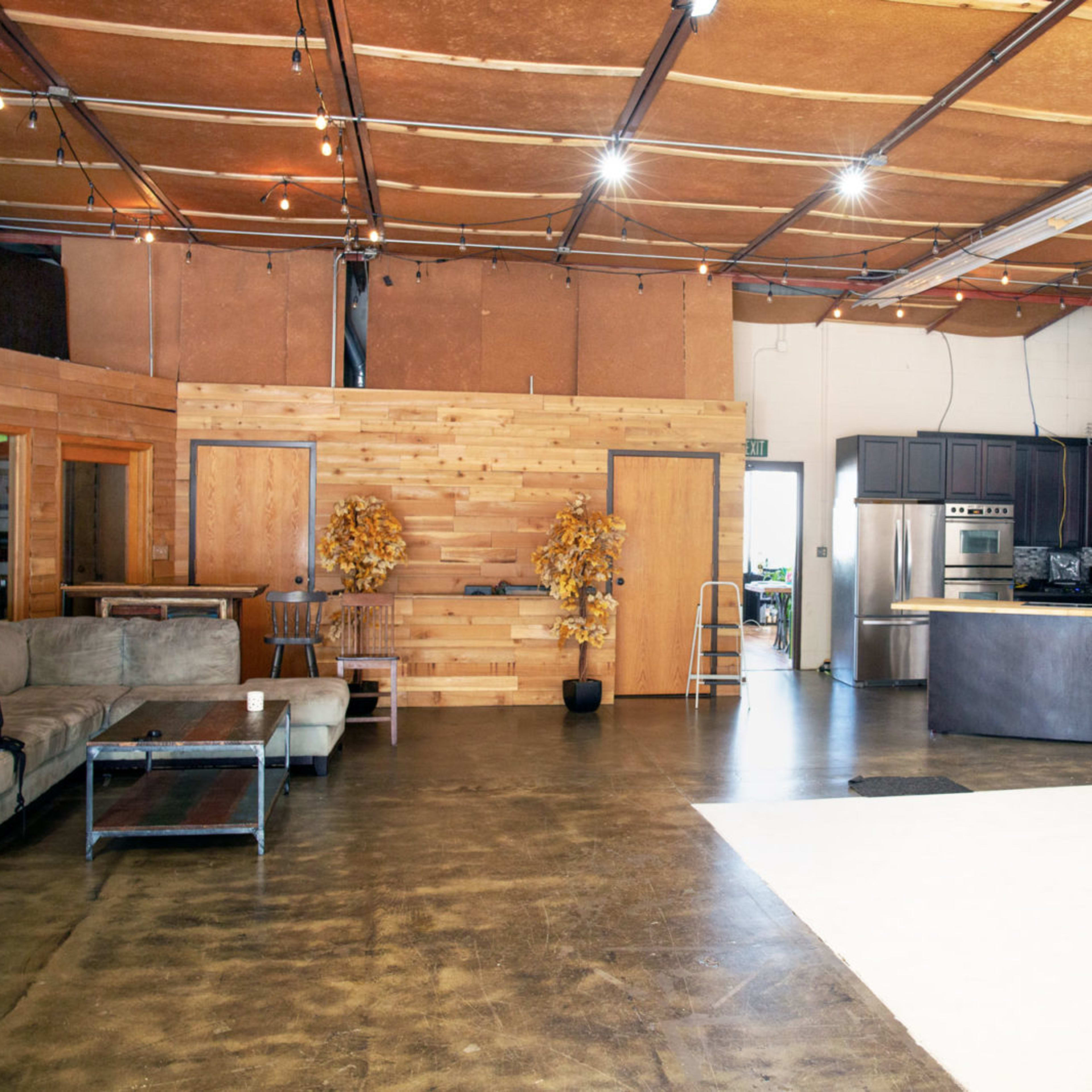 A spacious, industrial-style interior with exposed ceilings, a kitchen area, and a seating arrangement made of a couch and a coffee table.