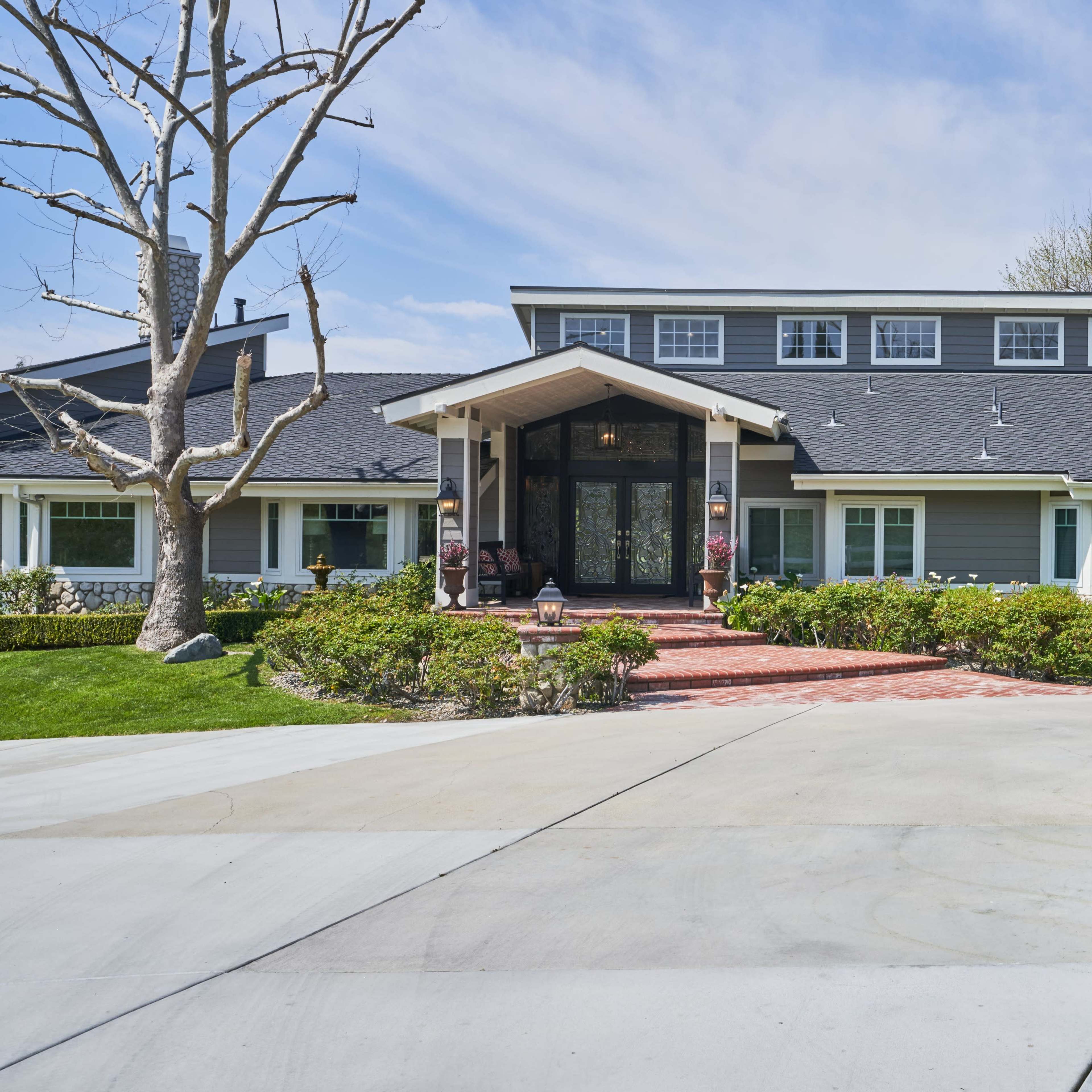 A large, modern house with a distinctive peaked entrance and a circular driveway surrounded by well-maintained landscaping.