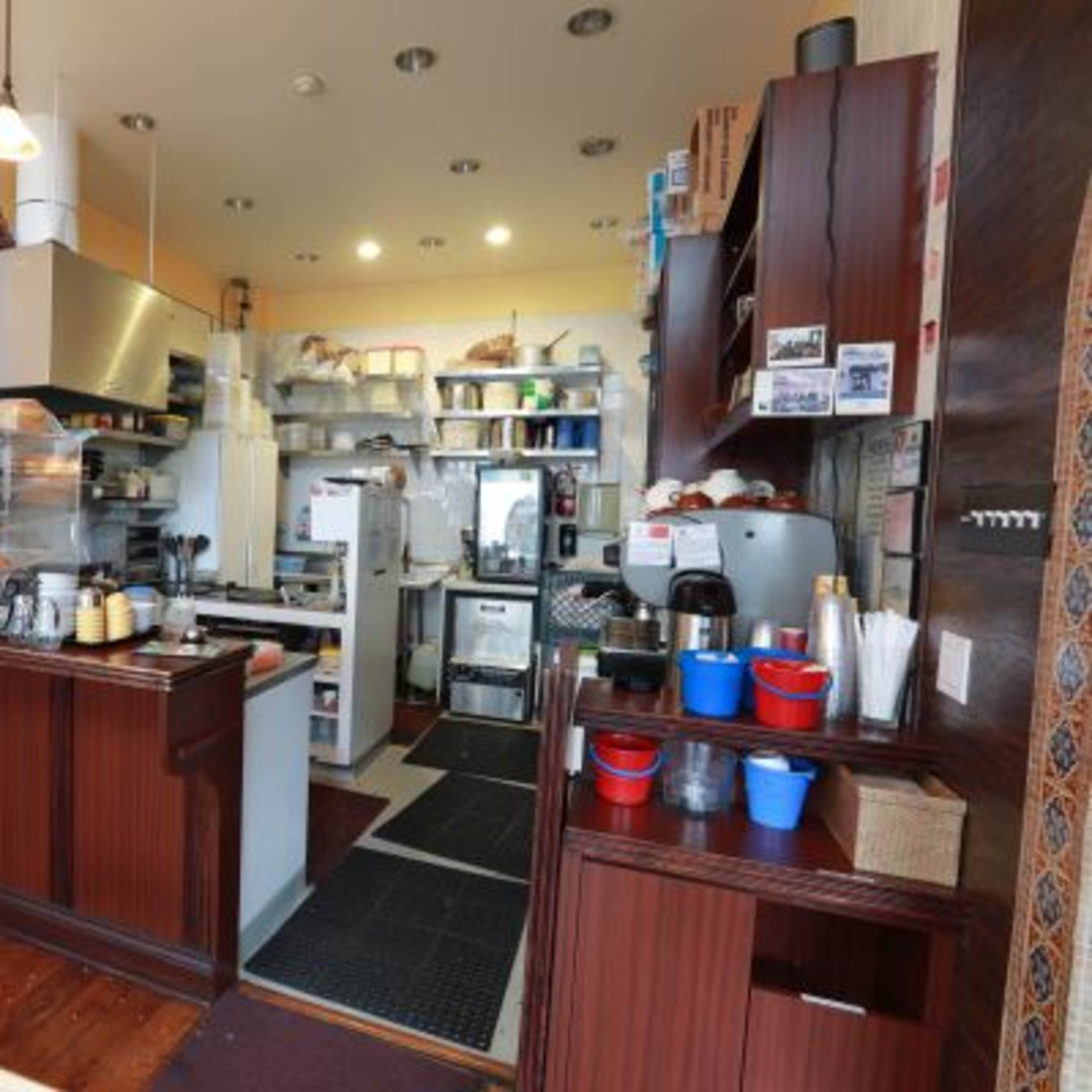 A small café interior with a countertop, coffee machines, and shelves filled with kitchen supplies.