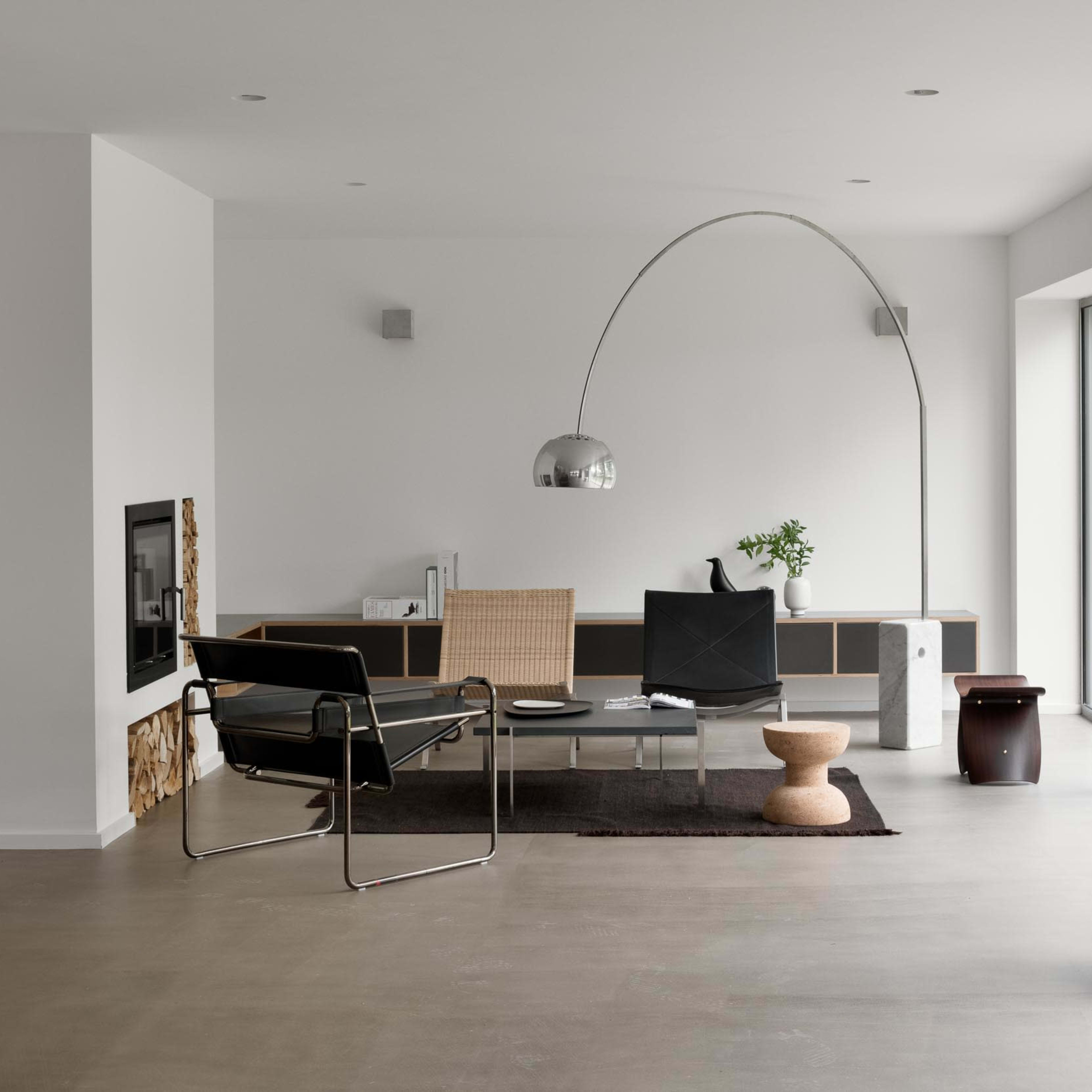 A modern living room with minimalist furniture, including a sleek chair, a coffee table, and large windows allowing natural light to fill the space.