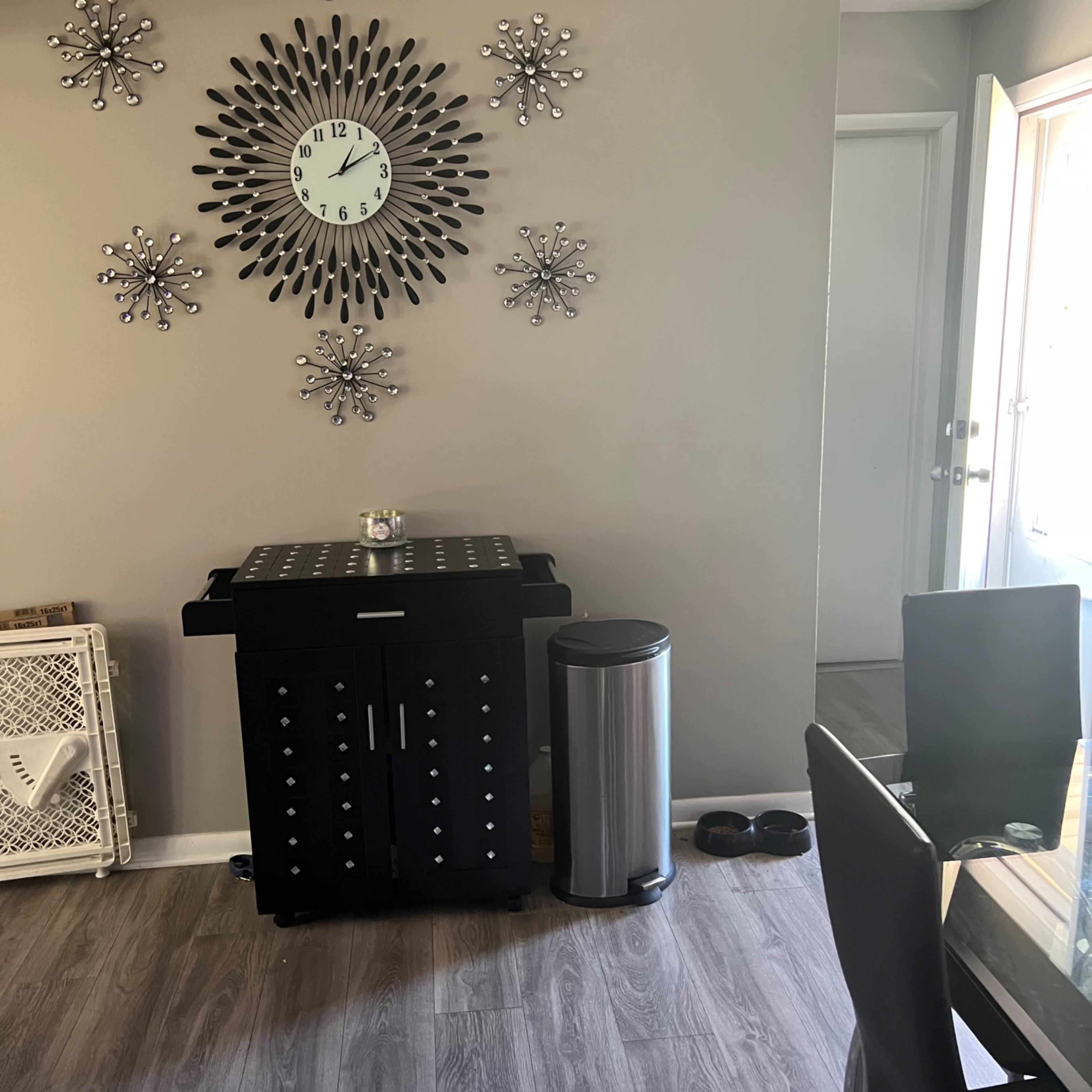 A modern dining area featuring a black cabinet, a silver trash can, a decorative wall clock, and star-shaped wall decorations.