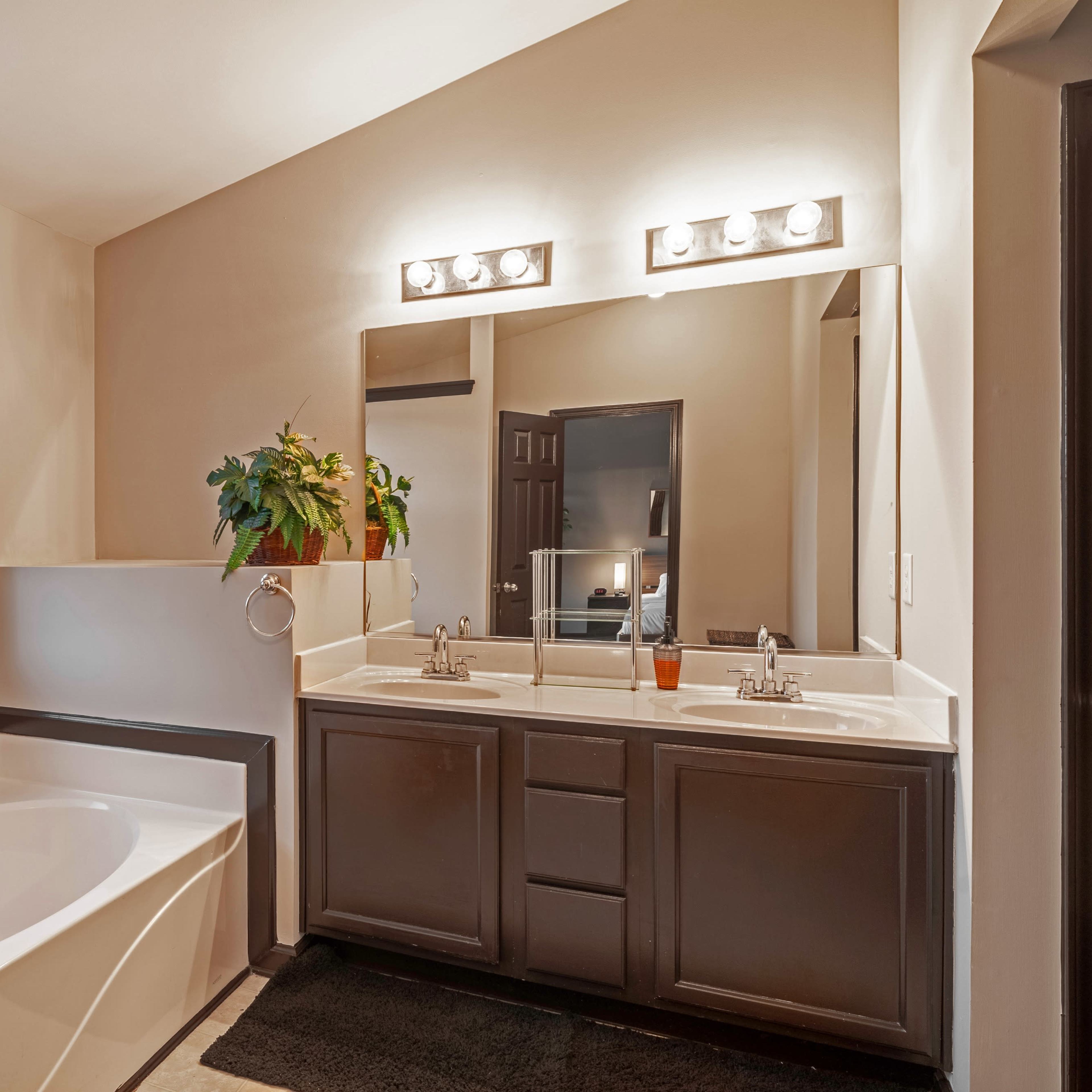 A bathroom featuring a bathtub, double vanity with sinks, and a window with potted plants on the countertop.