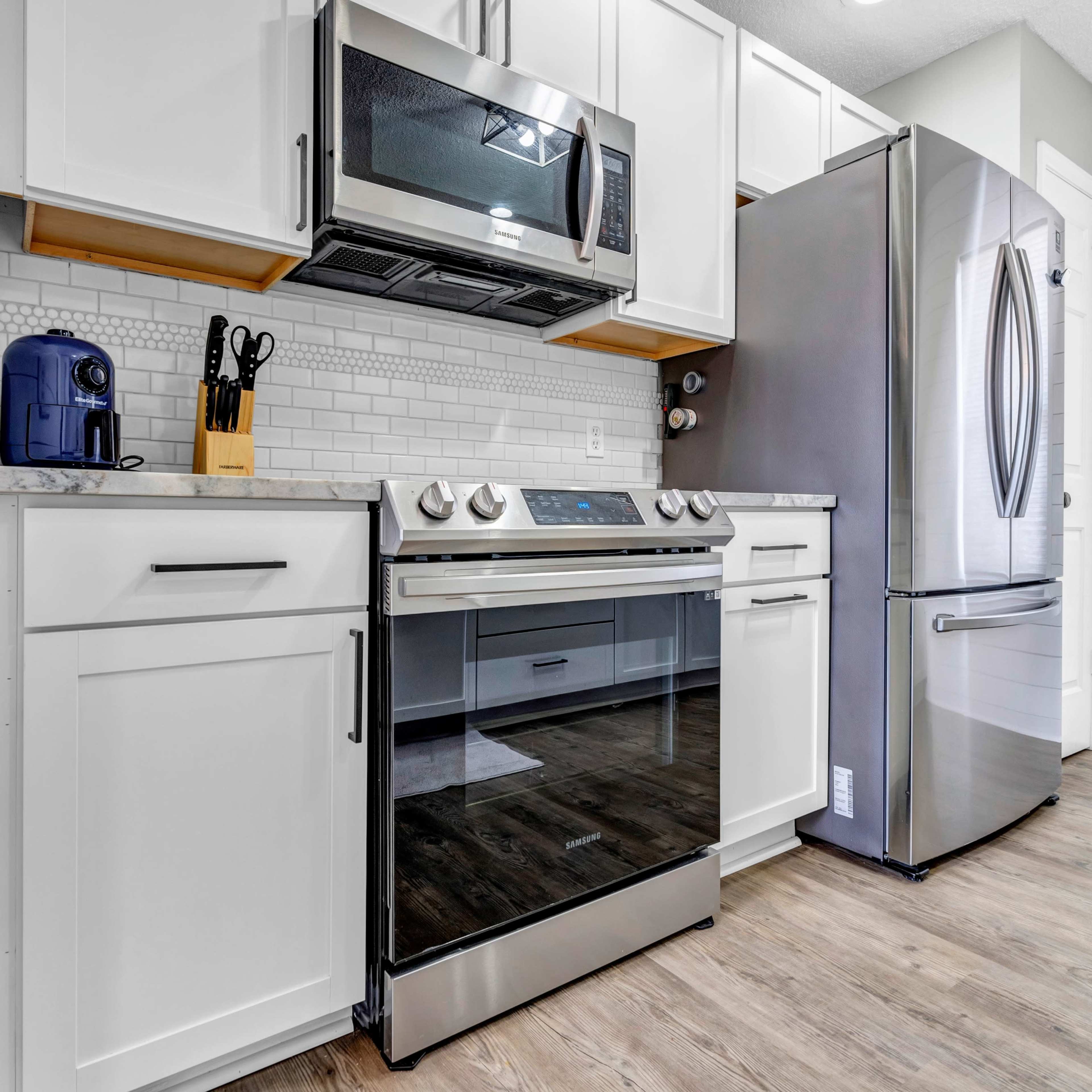 A modern kitchen featuring stainless steel appliances, including a microwave, oven, and refrigerator, set against white cabinetry and a tiled backsplash.