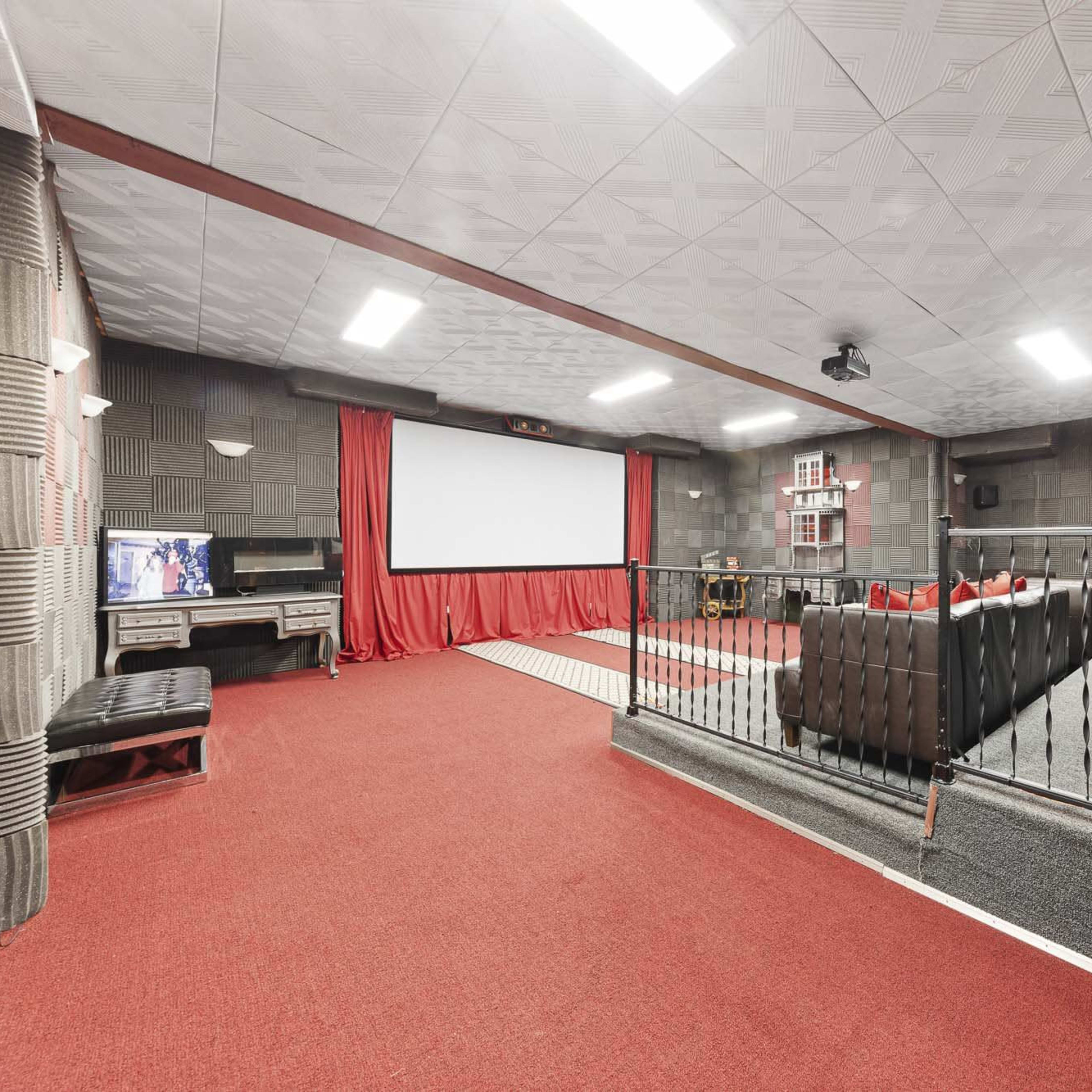 A home theater room with a large screen, comfortable seating, and red curtains.